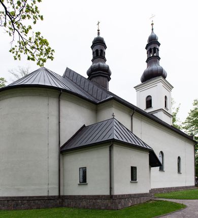 Zdjęcie nr 8: Kościół usytuowany jest w południowo-wschodniej części wsi, otoczony kamiennym murem, otynkowanym, krytym betonową płytą, w który wbudowano współczesne stacje drogi krzyżowej. Na plac kościelny prowadzą trzy bramy. Główna brama znajduje się w murze od strony zachodniej, nakryta jest ostrołukową arkadą. Dwie mniejsze bramy zlokalizowane są od strony południowej oraz od strony wschodniej. Na placu przed kościołem stoi pomnik z 1911 roku wystawiony na pamiątkę księdza Wojciecha Blaszyńskiego i działacza ludowego Stanisława Stojałowskiego. 
Świątynia jest orientowana, murowana, jednonawowa z węższym i krótkim prezbiterium, zamkniętym półkoliście oraz z wieżą na zakończeniu nawy. Do prezbiterium przylega zakrystia od północy i skarbczyk od południa. Od strony południowej dobudowana jest również niska kruchta. Wnętrze trójprzęsłowej nawy rozczłonkowane jest filarami przyściennymi wspierającymi sklepienie żagielkowe. Chór muzyczny trójarkadowy, wsparty na dwóch filarach. W ścianach korpusu nawowego znajdują się głębokie wnęki, w których umieszczone są prostokątne otwory okienne zamknięte półkolistym łukiem, po trzy od strony północnej i południowej; takie same okno znajduje się również w apsydzie od strony południowej oraz na chórze od strony zachodniej. Ponadto w apsydzie na wysokości zwieńczenia ołtarza głównego umieszczone jest małe, okrągłe okno. W kruchcie, skarbczyku i zakrystii okna są prostokątne. Drzwi główne dwuskrzydłowe, drewniane z metalowymi okuciami, zabezpieczone od wewnątrz dwiema żelaznymi zaporami umocowanymi w murze. Podobne drzwi znajdują się od strony południowej z kruchty. 
Fasada kościoła jest płaska, zakończona gzymsem z wysuniętą do przodu trójkondygnacyjną wieżą, nakrytą baniastym hełmem z latarnią. Drugie piętro wieży połączone jest z fasadą prostymi spływami. Przy wejściu na wysokich cokołach ustawione są rzeźby świętych Piotra i Pawła. 
Kościoł nakryty jest dachem dwuspadowym, na skrzyżowaniu nawy z prezbiterium umieszczona jest sygnaturka z hełmem baniastym z latarnią. 
