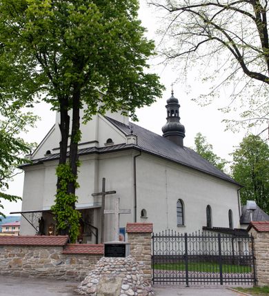 Zdjęcie nr 5: Kościół usytuowany jest w południowo-wschodniej części wsi, otoczony kamiennym murem, otynkowanym, krytym betonową płytą, w który wbudowano współczesne stacje drogi krzyżowej. Na plac kościelny prowadzą trzy bramy. Główna brama znajduje się w murze od strony zachodniej, nakryta jest ostrołukową arkadą. Dwie mniejsze bramy zlokalizowane są od strony południowej oraz od strony wschodniej. Na placu przed kościołem stoi pomnik z 1911 roku wystawiony na pamiątkę księdza Wojciecha Blaszyńskiego i działacza ludowego Stanisława Stojałowskiego. 
Świątynia jest orientowana, murowana, jednonawowa z węższym i krótkim prezbiterium, zamkniętym półkoliście oraz z wieżą na zakończeniu nawy. Do prezbiterium przylega zakrystia od północy i skarbczyk od południa. Od strony południowej dobudowana jest również niska kruchta. Wnętrze trójprzęsłowej nawy rozczłonkowane jest filarami przyściennymi wspierającymi sklepienie żagielkowe. Chór muzyczny trójarkadowy, wsparty na dwóch filarach. W ścianach korpusu nawowego znajdują się głębokie wnęki, w których umieszczone są prostokątne otwory okienne zamknięte półkolistym łukiem, po trzy od strony północnej i południowej; takie same okno znajduje się również w apsydzie od strony południowej oraz na chórze od strony zachodniej. Ponadto w apsydzie na wysokości zwieńczenia ołtarza głównego umieszczone jest małe, okrągłe okno. W kruchcie, skarbczyku i zakrystii okna są prostokątne. Drzwi główne dwuskrzydłowe, drewniane z metalowymi okuciami, zabezpieczone od wewnątrz dwiema żelaznymi zaporami umocowanymi w murze. Podobne drzwi znajdują się od strony południowej z kruchty. 
Fasada kościoła jest płaska, zakończona gzymsem z wysuniętą do przodu trójkondygnacyjną wieżą, nakrytą baniastym hełmem z latarnią. Drugie piętro wieży połączone jest z fasadą prostymi spływami. Przy wejściu na wysokich cokołach ustawione są rzeźby świętych Piotra i Pawła. 
Kościoł nakryty jest dachem dwuspadowym, na skrzyżowaniu nawy z prezbiterium umieszczona jest sygnaturka z hełmem baniastym z latarnią. 
