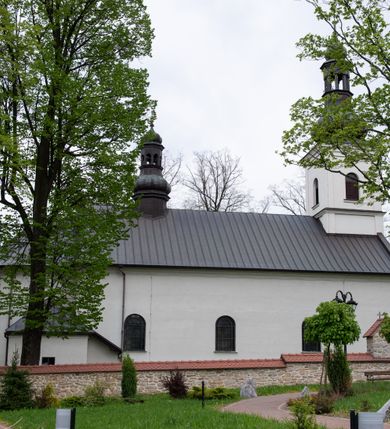 Zdjęcie nr 9: Kościół usytuowany jest w południowo-wschodniej części wsi, otoczony kamiennym murem, otynkowanym, krytym betonową płytą, w który wbudowano współczesne stacje drogi krzyżowej. Na plac kościelny prowadzą trzy bramy. Główna brama znajduje się w murze od strony zachodniej, nakryta jest ostrołukową arkadą. Dwie mniejsze bramy zlokalizowane są od strony południowej oraz od strony wschodniej. Na placu przed kościołem stoi pomnik z 1911 roku wystawiony na pamiątkę księdza Wojciecha Blaszyńskiego i działacza ludowego Stanisława Stojałowskiego. 
Świątynia jest orientowana, murowana, jednonawowa z węższym i krótkim prezbiterium, zamkniętym półkoliście oraz z wieżą na zakończeniu nawy. Do prezbiterium przylega zakrystia od północy i skarbczyk od południa. Od strony południowej dobudowana jest również niska kruchta. Wnętrze trójprzęsłowej nawy rozczłonkowane jest filarami przyściennymi wspierającymi sklepienie żagielkowe. Chór muzyczny trójarkadowy, wsparty na dwóch filarach. W ścianach korpusu nawowego znajdują się głębokie wnęki, w których umieszczone są prostokątne otwory okienne zamknięte półkolistym łukiem, po trzy od strony północnej i południowej; takie same okno znajduje się również w apsydzie od strony południowej oraz na chórze od strony zachodniej. Ponadto w apsydzie na wysokości zwieńczenia ołtarza głównego umieszczone jest małe, okrągłe okno. W kruchcie, skarbczyku i zakrystii okna są prostokątne. Drzwi główne dwuskrzydłowe, drewniane z metalowymi okuciami, zabezpieczone od wewnątrz dwiema żelaznymi zaporami umocowanymi w murze. Podobne drzwi znajdują się od strony południowej z kruchty. 
Fasada kościoła jest płaska, zakończona gzymsem z wysuniętą do przodu trójkondygnacyjną wieżą, nakrytą baniastym hełmem z latarnią. Drugie piętro wieży połączone jest z fasadą prostymi spływami. Przy wejściu na wysokich cokołach ustawione są rzeźby świętych Piotra i Pawła. 
Kościoł nakryty jest dachem dwuspadowym, na skrzyżowaniu nawy z prezbiterium umieszczona jest sygnaturka z hełmem baniastym z latarnią. 
