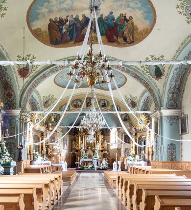 Zdjęcie nr 18: Kościół usytuowany jest w południowo-wschodniej części wsi, otoczony kamiennym murem, otynkowanym, krytym betonową płytą, w który wbudowano współczesne stacje drogi krzyżowej. Na plac kościelny prowadzą trzy bramy. Główna brama znajduje się w murze od strony zachodniej, nakryta jest ostrołukową arkadą. Dwie mniejsze bramy zlokalizowane są od strony południowej oraz od strony wschodniej. Na placu przed kościołem stoi pomnik z 1911 roku wystawiony na pamiątkę księdza Wojciecha Blaszyńskiego i działacza ludowego Stanisława Stojałowskiego. 
Świątynia jest orientowana, murowana, jednonawowa z węższym i krótkim prezbiterium, zamkniętym półkoliście oraz z wieżą na zakończeniu nawy. Do prezbiterium przylega zakrystia od północy i skarbczyk od południa. Od strony południowej dobudowana jest również niska kruchta. Wnętrze trójprzęsłowej nawy rozczłonkowane jest filarami przyściennymi wspierającymi sklepienie żagielkowe. Chór muzyczny trójarkadowy, wsparty na dwóch filarach. W ścianach korpusu nawowego znajdują się głębokie wnęki, w których umieszczone są prostokątne otwory okienne zamknięte półkolistym łukiem, po trzy od strony północnej i południowej; takie same okno znajduje się również w apsydzie od strony południowej oraz na chórze od strony zachodniej. Ponadto w apsydzie na wysokości zwieńczenia ołtarza głównego umieszczone jest małe, okrągłe okno. W kruchcie, skarbczyku i zakrystii okna są prostokątne. Drzwi główne dwuskrzydłowe, drewniane z metalowymi okuciami, zabezpieczone od wewnątrz dwiema żelaznymi zaporami umocowanymi w murze. Podobne drzwi znajdują się od strony południowej z kruchty. 
Fasada kościoła jest płaska, zakończona gzymsem z wysuniętą do przodu trójkondygnacyjną wieżą, nakrytą baniastym hełmem z latarnią. Drugie piętro wieży połączone jest z fasadą prostymi spływami. Przy wejściu na wysokich cokołach ustawione są rzeźby świętych Piotra i Pawła. 
Kościoł nakryty jest dachem dwuspadowym, na skrzyżowaniu nawy z prezbiterium umieszczona jest sygnaturka z hełmem baniastym z latarnią. 
