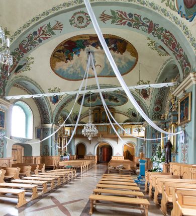 Zdjęcie nr 23: Kościół usytuowany jest w południowo-wschodniej części wsi, otoczony kamiennym murem, otynkowanym, krytym betonową płytą, w który wbudowano współczesne stacje drogi krzyżowej. Na plac kościelny prowadzą trzy bramy. Główna brama znajduje się w murze od strony zachodniej, nakryta jest ostrołukową arkadą. Dwie mniejsze bramy zlokalizowane są od strony południowej oraz od strony wschodniej. Na placu przed kościołem stoi pomnik z 1911 roku wystawiony na pamiątkę księdza Wojciecha Blaszyńskiego i działacza ludowego Stanisława Stojałowskiego. 
Świątynia jest orientowana, murowana, jednonawowa z węższym i krótkim prezbiterium, zamkniętym półkoliście oraz z wieżą na zakończeniu nawy. Do prezbiterium przylega zakrystia od północy i skarbczyk od południa. Od strony południowej dobudowana jest również niska kruchta. Wnętrze trójprzęsłowej nawy rozczłonkowane jest filarami przyściennymi wspierającymi sklepienie żagielkowe. Chór muzyczny trójarkadowy, wsparty na dwóch filarach. W ścianach korpusu nawowego znajdują się głębokie wnęki, w których umieszczone są prostokątne otwory okienne zamknięte półkolistym łukiem, po trzy od strony północnej i południowej; takie same okno znajduje się również w apsydzie od strony południowej oraz na chórze od strony zachodniej. Ponadto w apsydzie na wysokości zwieńczenia ołtarza głównego umieszczone jest małe, okrągłe okno. W kruchcie, skarbczyku i zakrystii okna są prostokątne. Drzwi główne dwuskrzydłowe, drewniane z metalowymi okuciami, zabezpieczone od wewnątrz dwiema żelaznymi zaporami umocowanymi w murze. Podobne drzwi znajdują się od strony południowej z kruchty. 
Fasada kościoła jest płaska, zakończona gzymsem z wysuniętą do przodu trójkondygnacyjną wieżą, nakrytą baniastym hełmem z latarnią. Drugie piętro wieży połączone jest z fasadą prostymi spływami. Przy wejściu na wysokich cokołach ustawione są rzeźby świętych Piotra i Pawła. 
Kościoł nakryty jest dachem dwuspadowym, na skrzyżowaniu nawy z prezbiterium umieszczona jest sygnaturka z hełmem baniastym z latarnią. 
