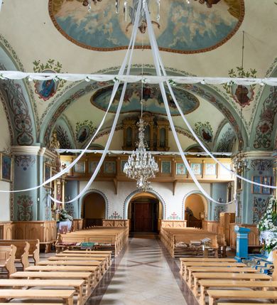 Zdjęcie nr 19: Kościół usytuowany jest w południowo-wschodniej części wsi, otoczony kamiennym murem, otynkowanym, krytym betonową płytą, w który wbudowano współczesne stacje drogi krzyżowej. Na plac kościelny prowadzą trzy bramy. Główna brama znajduje się w murze od strony zachodniej, nakryta jest ostrołukową arkadą. Dwie mniejsze bramy zlokalizowane są od strony południowej oraz od strony wschodniej. Na placu przed kościołem stoi pomnik z 1911 roku wystawiony na pamiątkę księdza Wojciecha Blaszyńskiego i działacza ludowego Stanisława Stojałowskiego. 
Świątynia jest orientowana, murowana, jednonawowa z węższym i krótkim prezbiterium, zamkniętym półkoliście oraz z wieżą na zakończeniu nawy. Do prezbiterium przylega zakrystia od północy i skarbczyk od południa. Od strony południowej dobudowana jest również niska kruchta. Wnętrze trójprzęsłowej nawy rozczłonkowane jest filarami przyściennymi wspierającymi sklepienie żagielkowe. Chór muzyczny trójarkadowy, wsparty na dwóch filarach. W ścianach korpusu nawowego znajdują się głębokie wnęki, w których umieszczone są prostokątne otwory okienne zamknięte półkolistym łukiem, po trzy od strony północnej i południowej; takie same okno znajduje się również w apsydzie od strony południowej oraz na chórze od strony zachodniej. Ponadto w apsydzie na wysokości zwieńczenia ołtarza głównego umieszczone jest małe, okrągłe okno. W kruchcie, skarbczyku i zakrystii okna są prostokątne. Drzwi główne dwuskrzydłowe, drewniane z metalowymi okuciami, zabezpieczone od wewnątrz dwiema żelaznymi zaporami umocowanymi w murze. Podobne drzwi znajdują się od strony południowej z kruchty. 
Fasada kościoła jest płaska, zakończona gzymsem z wysuniętą do przodu trójkondygnacyjną wieżą, nakrytą baniastym hełmem z latarnią. Drugie piętro wieży połączone jest z fasadą prostymi spływami. Przy wejściu na wysokich cokołach ustawione są rzeźby świętych Piotra i Pawła. 
Kościoł nakryty jest dachem dwuspadowym, na skrzyżowaniu nawy z prezbiterium umieszczona jest sygnaturka z hełmem baniastym z latarnią. 
