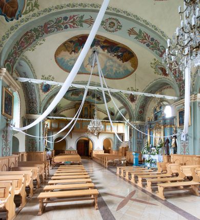 Zdjęcie nr 22: Kościół usytuowany jest w południowo-wschodniej części wsi, otoczony kamiennym murem, otynkowanym, krytym betonową płytą, w który wbudowano współczesne stacje drogi krzyżowej. Na plac kościelny prowadzą trzy bramy. Główna brama znajduje się w murze od strony zachodniej, nakryta jest ostrołukową arkadą. Dwie mniejsze bramy zlokalizowane są od strony południowej oraz od strony wschodniej. Na placu przed kościołem stoi pomnik z 1911 roku wystawiony na pamiątkę księdza Wojciecha Blaszyńskiego i działacza ludowego Stanisława Stojałowskiego. 
Świątynia jest orientowana, murowana, jednonawowa z węższym i krótkim prezbiterium, zamkniętym półkoliście oraz z wieżą na zakończeniu nawy. Do prezbiterium przylega zakrystia od północy i skarbczyk od południa. Od strony południowej dobudowana jest również niska kruchta. Wnętrze trójprzęsłowej nawy rozczłonkowane jest filarami przyściennymi wspierającymi sklepienie żagielkowe. Chór muzyczny trójarkadowy, wsparty na dwóch filarach. W ścianach korpusu nawowego znajdują się głębokie wnęki, w których umieszczone są prostokątne otwory okienne zamknięte półkolistym łukiem, po trzy od strony północnej i południowej; takie same okno znajduje się również w apsydzie od strony południowej oraz na chórze od strony zachodniej. Ponadto w apsydzie na wysokości zwieńczenia ołtarza głównego umieszczone jest małe, okrągłe okno. W kruchcie, skarbczyku i zakrystii okna są prostokątne. Drzwi główne dwuskrzydłowe, drewniane z metalowymi okuciami, zabezpieczone od wewnątrz dwiema żelaznymi zaporami umocowanymi w murze. Podobne drzwi znajdują się od strony południowej z kruchty. 
Fasada kościoła jest płaska, zakończona gzymsem z wysuniętą do przodu trójkondygnacyjną wieżą, nakrytą baniastym hełmem z latarnią. Drugie piętro wieży połączone jest z fasadą prostymi spływami. Przy wejściu na wysokich cokołach ustawione są rzeźby świętych Piotra i Pawła. 
Kościoł nakryty jest dachem dwuspadowym, na skrzyżowaniu nawy z prezbiterium umieszczona jest sygnaturka z hełmem baniastym z latarnią. 
