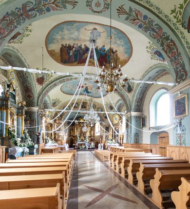 Zdjęcie nr 21: Kościół usytuowany jest w południowo-wschodniej części wsi, otoczony kamiennym murem, otynkowanym, krytym betonową płytą, w który wbudowano współczesne stacje drogi krzyżowej. Na plac kościelny prowadzą trzy bramy. Główna brama znajduje się w murze od strony zachodniej, nakryta jest ostrołukową arkadą. Dwie mniejsze bramy zlokalizowane są od strony południowej oraz od strony wschodniej. Na placu przed kościołem stoi pomnik z 1911 roku wystawiony na pamiątkę księdza Wojciecha Blaszyńskiego i działacza ludowego Stanisława Stojałowskiego. 
Świątynia jest orientowana, murowana, jednonawowa z węższym i krótkim prezbiterium, zamkniętym półkoliście oraz z wieżą na zakończeniu nawy. Do prezbiterium przylega zakrystia od północy i skarbczyk od południa. Od strony południowej dobudowana jest również niska kruchta. Wnętrze trójprzęsłowej nawy rozczłonkowane jest filarami przyściennymi wspierającymi sklepienie żagielkowe. Chór muzyczny trójarkadowy, wsparty na dwóch filarach. W ścianach korpusu nawowego znajdują się głębokie wnęki, w których umieszczone są prostokątne otwory okienne zamknięte półkolistym łukiem, po trzy od strony północnej i południowej; takie same okno znajduje się również w apsydzie od strony południowej oraz na chórze od strony zachodniej. Ponadto w apsydzie na wysokości zwieńczenia ołtarza głównego umieszczone jest małe, okrągłe okno. W kruchcie, skarbczyku i zakrystii okna są prostokątne. Drzwi główne dwuskrzydłowe, drewniane z metalowymi okuciami, zabezpieczone od wewnątrz dwiema żelaznymi zaporami umocowanymi w murze. Podobne drzwi znajdują się od strony południowej z kruchty. 
Fasada kościoła jest płaska, zakończona gzymsem z wysuniętą do przodu trójkondygnacyjną wieżą, nakrytą baniastym hełmem z latarnią. Drugie piętro wieży połączone jest z fasadą prostymi spływami. Przy wejściu na wysokich cokołach ustawione są rzeźby świętych Piotra i Pawła. 
Kościoł nakryty jest dachem dwuspadowym, na skrzyżowaniu nawy z prezbiterium umieszczona jest sygnaturka z hełmem baniastym z latarnią. 
