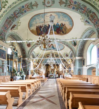 Zdjęcie nr 20: Kościół usytuowany jest w południowo-wschodniej części wsi, otoczony kamiennym murem, otynkowanym, krytym betonową płytą, w który wbudowano współczesne stacje drogi krzyżowej. Na plac kościelny prowadzą trzy bramy. Główna brama znajduje się w murze od strony zachodniej, nakryta jest ostrołukową arkadą. Dwie mniejsze bramy zlokalizowane są od strony południowej oraz od strony wschodniej. Na placu przed kościołem stoi pomnik z 1911 roku wystawiony na pamiątkę księdza Wojciecha Blaszyńskiego i działacza ludowego Stanisława Stojałowskiego. 
Świątynia jest orientowana, murowana, jednonawowa z węższym i krótkim prezbiterium, zamkniętym półkoliście oraz z wieżą na zakończeniu nawy. Do prezbiterium przylega zakrystia od północy i skarbczyk od południa. Od strony południowej dobudowana jest również niska kruchta. Wnętrze trójprzęsłowej nawy rozczłonkowane jest filarami przyściennymi wspierającymi sklepienie żagielkowe. Chór muzyczny trójarkadowy, wsparty na dwóch filarach. W ścianach korpusu nawowego znajdują się głębokie wnęki, w których umieszczone są prostokątne otwory okienne zamknięte półkolistym łukiem, po trzy od strony północnej i południowej; takie same okno znajduje się również w apsydzie od strony południowej oraz na chórze od strony zachodniej. Ponadto w apsydzie na wysokości zwieńczenia ołtarza głównego umieszczone jest małe, okrągłe okno. W kruchcie, skarbczyku i zakrystii okna są prostokątne. Drzwi główne dwuskrzydłowe, drewniane z metalowymi okuciami, zabezpieczone od wewnątrz dwiema żelaznymi zaporami umocowanymi w murze. Podobne drzwi znajdują się od strony południowej z kruchty. 
Fasada kościoła jest płaska, zakończona gzymsem z wysuniętą do przodu trójkondygnacyjną wieżą, nakrytą baniastym hełmem z latarnią. Drugie piętro wieży połączone jest z fasadą prostymi spływami. Przy wejściu na wysokich cokołach ustawione są rzeźby świętych Piotra i Pawła. 
Kościoł nakryty jest dachem dwuspadowym, na skrzyżowaniu nawy z prezbiterium umieszczona jest sygnaturka z hełmem baniastym z latarnią. 
