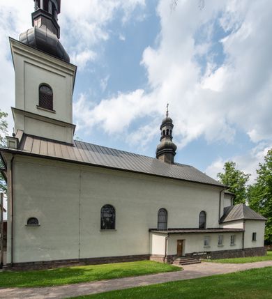 Zdjęcie nr 2: Kościół usytuowany jest w południowo-wschodniej części wsi, otoczony kamiennym murem, otynkowanym, krytym betonową płytą, w który wbudowano współczesne stacje drogi krzyżowej. Na plac kościelny prowadzą trzy bramy. Główna brama znajduje się w murze od strony zachodniej, nakryta jest ostrołukową arkadą. Dwie mniejsze bramy zlokalizowane są od strony południowej oraz od strony wschodniej. Na placu przed kościołem stoi pomnik z 1911 roku wystawiony na pamiątkę księdza Wojciecha Blaszyńskiego i działacza ludowego Stanisława Stojałowskiego. 
Świątynia jest orientowana, murowana, jednonawowa z węższym i krótkim prezbiterium, zamkniętym półkoliście oraz z wieżą na zakończeniu nawy. Do prezbiterium przylega zakrystia od północy i skarbczyk od południa. Od strony południowej dobudowana jest również niska kruchta. Wnętrze trójprzęsłowej nawy rozczłonkowane jest filarami przyściennymi wspierającymi sklepienie żagielkowe. Chór muzyczny trójarkadowy, wsparty na dwóch filarach. W ścianach korpusu nawowego znajdują się głębokie wnęki, w których umieszczone są prostokątne otwory okienne zamknięte półkolistym łukiem, po trzy od strony północnej i południowej; takie same okno znajduje się również w apsydzie od strony południowej oraz na chórze od strony zachodniej. Ponadto w apsydzie na wysokości zwieńczenia ołtarza głównego umieszczone jest małe, okrągłe okno. W kruchcie, skarbczyku i zakrystii okna są prostokątne. Drzwi główne dwuskrzydłowe, drewniane z metalowymi okuciami, zabezpieczone od wewnątrz dwiema żelaznymi zaporami umocowanymi w murze. Podobne drzwi znajdują się od strony południowej z kruchty. 
Fasada kościoła jest płaska, zakończona gzymsem z wysuniętą do przodu trójkondygnacyjną wieżą, nakrytą baniastym hełmem z latarnią. Drugie piętro wieży połączone jest z fasadą prostymi spływami. Przy wejściu na wysokich cokołach ustawione są rzeźby świętych Piotra i Pawła. 
Kościoł nakryty jest dachem dwuspadowym, na skrzyżowaniu nawy z prezbiterium umieszczona jest sygnaturka z hełmem baniastym z latarnią. 
