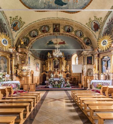 Zdjęcie nr 27: Kościół usytuowany jest w południowo-wschodniej części wsi, otoczony kamiennym murem, otynkowanym, krytym betonową płytą, w który wbudowano współczesne stacje drogi krzyżowej. Na plac kościelny prowadzą trzy bramy. Główna brama znajduje się w murze od strony zachodniej, nakryta jest ostrołukową arkadą. Dwie mniejsze bramy zlokalizowane są od strony południowej oraz od strony wschodniej. Na placu przed kościołem stoi pomnik z 1911 roku wystawiony na pamiątkę księdza Wojciecha Blaszyńskiego i działacza ludowego Stanisława Stojałowskiego. 
Świątynia jest orientowana, murowana, jednonawowa z węższym i krótkim prezbiterium, zamkniętym półkoliście oraz z wieżą na zakończeniu nawy. Do prezbiterium przylega zakrystia od północy i skarbczyk od południa. Od strony południowej dobudowana jest również niska kruchta. Wnętrze trójprzęsłowej nawy rozczłonkowane jest filarami przyściennymi wspierającymi sklepienie żagielkowe. Chór muzyczny trójarkadowy, wsparty na dwóch filarach. W ścianach korpusu nawowego znajdują się głębokie wnęki, w których umieszczone są prostokątne otwory okienne zamknięte półkolistym łukiem, po trzy od strony północnej i południowej; takie same okno znajduje się również w apsydzie od strony południowej oraz na chórze od strony zachodniej. Ponadto w apsydzie na wysokości zwieńczenia ołtarza głównego umieszczone jest małe, okrągłe okno. W kruchcie, skarbczyku i zakrystii okna są prostokątne. Drzwi główne dwuskrzydłowe, drewniane z metalowymi okuciami, zabezpieczone od wewnątrz dwiema żelaznymi zaporami umocowanymi w murze. Podobne drzwi znajdują się od strony południowej z kruchty. 
Fasada kościoła jest płaska, zakończona gzymsem z wysuniętą do przodu trójkondygnacyjną wieżą, nakrytą baniastym hełmem z latarnią. Drugie piętro wieży połączone jest z fasadą prostymi spływami. Przy wejściu na wysokich cokołach ustawione są rzeźby świętych Piotra i Pawła. 
Kościoł nakryty jest dachem dwuspadowym, na skrzyżowaniu nawy z prezbiterium umieszczona jest sygnaturka z hełmem baniastym z latarnią. 
