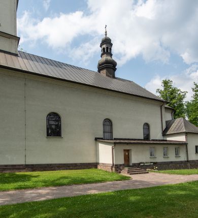 Zdjęcie nr 3: Kościół usytuowany jest w południowo-wschodniej części wsi, otoczony kamiennym murem, otynkowanym, krytym betonową płytą, w który wbudowano współczesne stacje drogi krzyżowej. Na plac kościelny prowadzą trzy bramy. Główna brama znajduje się w murze od strony zachodniej, nakryta jest ostrołukową arkadą. Dwie mniejsze bramy zlokalizowane są od strony południowej oraz od strony wschodniej. Na placu przed kościołem stoi pomnik z 1911 roku wystawiony na pamiątkę księdza Wojciecha Blaszyńskiego i działacza ludowego Stanisława Stojałowskiego. 
Świątynia jest orientowana, murowana, jednonawowa z węższym i krótkim prezbiterium, zamkniętym półkoliście oraz z wieżą na zakończeniu nawy. Do prezbiterium przylega zakrystia od północy i skarbczyk od południa. Od strony południowej dobudowana jest również niska kruchta. Wnętrze trójprzęsłowej nawy rozczłonkowane jest filarami przyściennymi wspierającymi sklepienie żagielkowe. Chór muzyczny trójarkadowy, wsparty na dwóch filarach. W ścianach korpusu nawowego znajdują się głębokie wnęki, w których umieszczone są prostokątne otwory okienne zamknięte półkolistym łukiem, po trzy od strony północnej i południowej; takie same okno znajduje się również w apsydzie od strony południowej oraz na chórze od strony zachodniej. Ponadto w apsydzie na wysokości zwieńczenia ołtarza głównego umieszczone jest małe, okrągłe okno. W kruchcie, skarbczyku i zakrystii okna są prostokątne. Drzwi główne dwuskrzydłowe, drewniane z metalowymi okuciami, zabezpieczone od wewnątrz dwiema żelaznymi zaporami umocowanymi w murze. Podobne drzwi znajdują się od strony południowej z kruchty. 
Fasada kościoła jest płaska, zakończona gzymsem z wysuniętą do przodu trójkondygnacyjną wieżą, nakrytą baniastym hełmem z latarnią. Drugie piętro wieży połączone jest z fasadą prostymi spływami. Przy wejściu na wysokich cokołach ustawione są rzeźby świętych Piotra i Pawła. 
Kościoł nakryty jest dachem dwuspadowym, na skrzyżowaniu nawy z prezbiterium umieszczona jest sygnaturka z hełmem baniastym z latarnią. 
