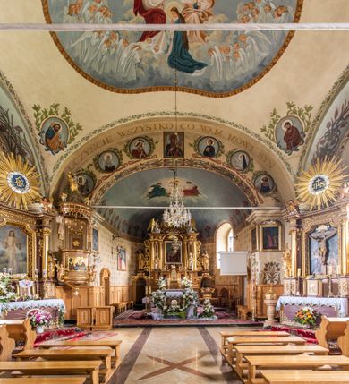 Zdjęcie nr 28: Kościół usytuowany jest w południowo-wschodniej części wsi, otoczony kamiennym murem, otynkowanym, krytym betonową płytą, w który wbudowano współczesne stacje drogi krzyżowej. Na plac kościelny prowadzą trzy bramy. Główna brama znajduje się w murze od strony zachodniej, nakryta jest ostrołukową arkadą. Dwie mniejsze bramy zlokalizowane są od strony południowej oraz od strony wschodniej. Na placu przed kościołem stoi pomnik z 1911 roku wystawiony na pamiątkę księdza Wojciecha Blaszyńskiego i działacza ludowego Stanisława Stojałowskiego. 
Świątynia jest orientowana, murowana, jednonawowa z węższym i krótkim prezbiterium, zamkniętym półkoliście oraz z wieżą na zakończeniu nawy. Do prezbiterium przylega zakrystia od północy i skarbczyk od południa. Od strony południowej dobudowana jest również niska kruchta. Wnętrze trójprzęsłowej nawy rozczłonkowane jest filarami przyściennymi wspierającymi sklepienie żagielkowe. Chór muzyczny trójarkadowy, wsparty na dwóch filarach. W ścianach korpusu nawowego znajdują się głębokie wnęki, w których umieszczone są prostokątne otwory okienne zamknięte półkolistym łukiem, po trzy od strony północnej i południowej; takie same okno znajduje się również w apsydzie od strony południowej oraz na chórze od strony zachodniej. Ponadto w apsydzie na wysokości zwieńczenia ołtarza głównego umieszczone jest małe, okrągłe okno. W kruchcie, skarbczyku i zakrystii okna są prostokątne. Drzwi główne dwuskrzydłowe, drewniane z metalowymi okuciami, zabezpieczone od wewnątrz dwiema żelaznymi zaporami umocowanymi w murze. Podobne drzwi znajdują się od strony południowej z kruchty. 
Fasada kościoła jest płaska, zakończona gzymsem z wysuniętą do przodu trójkondygnacyjną wieżą, nakrytą baniastym hełmem z latarnią. Drugie piętro wieży połączone jest z fasadą prostymi spływami. Przy wejściu na wysokich cokołach ustawione są rzeźby świętych Piotra i Pawła. 
Kościoł nakryty jest dachem dwuspadowym, na skrzyżowaniu nawy z prezbiterium umieszczona jest sygnaturka z hełmem baniastym z latarnią. 
