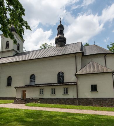 Zdjęcie nr 11: Kościół usytuowany jest w południowo-wschodniej części wsi, otoczony kamiennym murem, otynkowanym, krytym betonową płytą, w który wbudowano współczesne stacje drogi krzyżowej. Na plac kościelny prowadzą trzy bramy. Główna brama znajduje się w murze od strony zachodniej, nakryta jest ostrołukową arkadą. Dwie mniejsze bramy zlokalizowane są od strony południowej oraz od strony wschodniej. Na placu przed kościołem stoi pomnik z 1911 roku wystawiony na pamiątkę księdza Wojciecha Blaszyńskiego i działacza ludowego Stanisława Stojałowskiego. 
Świątynia jest orientowana, murowana, jednonawowa z węższym i krótkim prezbiterium, zamkniętym półkoliście oraz z wieżą na zakończeniu nawy. Do prezbiterium przylega zakrystia od północy i skarbczyk od południa. Od strony południowej dobudowana jest również niska kruchta. Wnętrze trójprzęsłowej nawy rozczłonkowane jest filarami przyściennymi wspierającymi sklepienie żagielkowe. Chór muzyczny trójarkadowy, wsparty na dwóch filarach. W ścianach korpusu nawowego znajdują się głębokie wnęki, w których umieszczone są prostokątne otwory okienne zamknięte półkolistym łukiem, po trzy od strony północnej i południowej; takie same okno znajduje się również w apsydzie od strony południowej oraz na chórze od strony zachodniej. Ponadto w apsydzie na wysokości zwieńczenia ołtarza głównego umieszczone jest małe, okrągłe okno. W kruchcie, skarbczyku i zakrystii okna są prostokątne. Drzwi główne dwuskrzydłowe, drewniane z metalowymi okuciami, zabezpieczone od wewnątrz dwiema żelaznymi zaporami umocowanymi w murze. Podobne drzwi znajdują się od strony południowej z kruchty. 
Fasada kościoła jest płaska, zakończona gzymsem z wysuniętą do przodu trójkondygnacyjną wieżą, nakrytą baniastym hełmem z latarnią. Drugie piętro wieży połączone jest z fasadą prostymi spływami. Przy wejściu na wysokich cokołach ustawione są rzeźby świętych Piotra i Pawła. 
Kościoł nakryty jest dachem dwuspadowym, na skrzyżowaniu nawy z prezbiterium umieszczona jest sygnaturka z hełmem baniastym z latarnią. 
