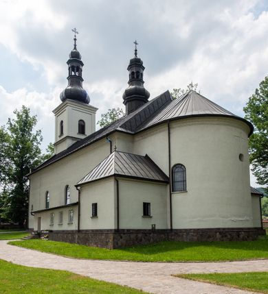 Zdjęcie nr 4: Kościół usytuowany jest w południowo-wschodniej części wsi, otoczony kamiennym murem, otynkowanym, krytym betonową płytą, w który wbudowano współczesne stacje drogi krzyżowej. Na plac kościelny prowadzą trzy bramy. Główna brama znajduje się w murze od strony zachodniej, nakryta jest ostrołukową arkadą. Dwie mniejsze bramy zlokalizowane są od strony południowej oraz od strony wschodniej. Na placu przed kościołem stoi pomnik z 1911 roku wystawiony na pamiątkę księdza Wojciecha Blaszyńskiego i działacza ludowego Stanisława Stojałowskiego. 
Świątynia jest orientowana, murowana, jednonawowa z węższym i krótkim prezbiterium, zamkniętym półkoliście oraz z wieżą na zakończeniu nawy. Do prezbiterium przylega zakrystia od północy i skarbczyk od południa. Od strony południowej dobudowana jest również niska kruchta. Wnętrze trójprzęsłowej nawy rozczłonkowane jest filarami przyściennymi wspierającymi sklepienie żagielkowe. Chór muzyczny trójarkadowy, wsparty na dwóch filarach. W ścianach korpusu nawowego znajdują się głębokie wnęki, w których umieszczone są prostokątne otwory okienne zamknięte półkolistym łukiem, po trzy od strony północnej i południowej; takie same okno znajduje się również w apsydzie od strony południowej oraz na chórze od strony zachodniej. Ponadto w apsydzie na wysokości zwieńczenia ołtarza głównego umieszczone jest małe, okrągłe okno. W kruchcie, skarbczyku i zakrystii okna są prostokątne. Drzwi główne dwuskrzydłowe, drewniane z metalowymi okuciami, zabezpieczone od wewnątrz dwiema żelaznymi zaporami umocowanymi w murze. Podobne drzwi znajdują się od strony południowej z kruchty. 
Fasada kościoła jest płaska, zakończona gzymsem z wysuniętą do przodu trójkondygnacyjną wieżą, nakrytą baniastym hełmem z latarnią. Drugie piętro wieży połączone jest z fasadą prostymi spływami. Przy wejściu na wysokich cokołach ustawione są rzeźby świętych Piotra i Pawła. 
Kościoł nakryty jest dachem dwuspadowym, na skrzyżowaniu nawy z prezbiterium umieszczona jest sygnaturka z hełmem baniastym z latarnią. 
