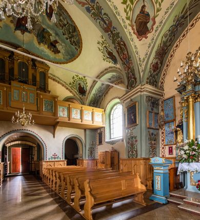 Zdjęcie nr 32: Kościół usytuowany jest w południowo-wschodniej części wsi, otoczony kamiennym murem, otynkowanym, krytym betonową płytą, w który wbudowano współczesne stacje drogi krzyżowej. Na plac kościelny prowadzą trzy bramy. Główna brama znajduje się w murze od strony zachodniej, nakryta jest ostrołukową arkadą. Dwie mniejsze bramy zlokalizowane są od strony południowej oraz od strony wschodniej. Na placu przed kościołem stoi pomnik z 1911 roku wystawiony na pamiątkę księdza Wojciecha Blaszyńskiego i działacza ludowego Stanisława Stojałowskiego. 
Świątynia jest orientowana, murowana, jednonawowa z węższym i krótkim prezbiterium, zamkniętym półkoliście oraz z wieżą na zakończeniu nawy. Do prezbiterium przylega zakrystia od północy i skarbczyk od południa. Od strony południowej dobudowana jest również niska kruchta. Wnętrze trójprzęsłowej nawy rozczłonkowane jest filarami przyściennymi wspierającymi sklepienie żagielkowe. Chór muzyczny trójarkadowy, wsparty na dwóch filarach. W ścianach korpusu nawowego znajdują się głębokie wnęki, w których umieszczone są prostokątne otwory okienne zamknięte półkolistym łukiem, po trzy od strony północnej i południowej; takie same okno znajduje się również w apsydzie od strony południowej oraz na chórze od strony zachodniej. Ponadto w apsydzie na wysokości zwieńczenia ołtarza głównego umieszczone jest małe, okrągłe okno. W kruchcie, skarbczyku i zakrystii okna są prostokątne. Drzwi główne dwuskrzydłowe, drewniane z metalowymi okuciami, zabezpieczone od wewnątrz dwiema żelaznymi zaporami umocowanymi w murze. Podobne drzwi znajdują się od strony południowej z kruchty. 
Fasada kościoła jest płaska, zakończona gzymsem z wysuniętą do przodu trójkondygnacyjną wieżą, nakrytą baniastym hełmem z latarnią. Drugie piętro wieży połączone jest z fasadą prostymi spływami. Przy wejściu na wysokich cokołach ustawione są rzeźby świętych Piotra i Pawła. 
Kościoł nakryty jest dachem dwuspadowym, na skrzyżowaniu nawy z prezbiterium umieszczona jest sygnaturka z hełmem baniastym z latarnią. 
