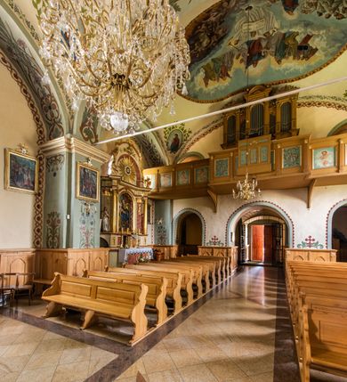 Zdjęcie nr 30: Kościół usytuowany jest w południowo-wschodniej części wsi, otoczony kamiennym murem, otynkowanym, krytym betonową płytą, w który wbudowano współczesne stacje drogi krzyżowej. Na plac kościelny prowadzą trzy bramy. Główna brama znajduje się w murze od strony zachodniej, nakryta jest ostrołukową arkadą. Dwie mniejsze bramy zlokalizowane są od strony południowej oraz od strony wschodniej. Na placu przed kościołem stoi pomnik z 1911 roku wystawiony na pamiątkę księdza Wojciecha Blaszyńskiego i działacza ludowego Stanisława Stojałowskiego. 
Świątynia jest orientowana, murowana, jednonawowa z węższym i krótkim prezbiterium, zamkniętym półkoliście oraz z wieżą na zakończeniu nawy. Do prezbiterium przylega zakrystia od północy i skarbczyk od południa. Od strony południowej dobudowana jest również niska kruchta. Wnętrze trójprzęsłowej nawy rozczłonkowane jest filarami przyściennymi wspierającymi sklepienie żagielkowe. Chór muzyczny trójarkadowy, wsparty na dwóch filarach. W ścianach korpusu nawowego znajdują się głębokie wnęki, w których umieszczone są prostokątne otwory okienne zamknięte półkolistym łukiem, po trzy od strony północnej i południowej; takie same okno znajduje się również w apsydzie od strony południowej oraz na chórze od strony zachodniej. Ponadto w apsydzie na wysokości zwieńczenia ołtarza głównego umieszczone jest małe, okrągłe okno. W kruchcie, skarbczyku i zakrystii okna są prostokątne. Drzwi główne dwuskrzydłowe, drewniane z metalowymi okuciami, zabezpieczone od wewnątrz dwiema żelaznymi zaporami umocowanymi w murze. Podobne drzwi znajdują się od strony południowej z kruchty. 
Fasada kościoła jest płaska, zakończona gzymsem z wysuniętą do przodu trójkondygnacyjną wieżą, nakrytą baniastym hełmem z latarnią. Drugie piętro wieży połączone jest z fasadą prostymi spływami. Przy wejściu na wysokich cokołach ustawione są rzeźby świętych Piotra i Pawła. 
Kościoł nakryty jest dachem dwuspadowym, na skrzyżowaniu nawy z prezbiterium umieszczona jest sygnaturka z hełmem baniastym z latarnią. 
