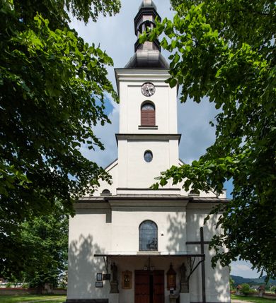 Zdjęcie nr 14: Kościół usytuowany jest w południowo-wschodniej części wsi, otoczony kamiennym murem, otynkowanym, krytym betonową płytą, w który wbudowano współczesne stacje drogi krzyżowej. Na plac kościelny prowadzą trzy bramy. Główna brama znajduje się w murze od strony zachodniej, nakryta jest ostrołukową arkadą. Dwie mniejsze bramy zlokalizowane są od strony południowej oraz od strony wschodniej. Na placu przed kościołem stoi pomnik z 1911 roku wystawiony na pamiątkę księdza Wojciecha Blaszyńskiego i działacza ludowego Stanisława Stojałowskiego. 
Świątynia jest orientowana, murowana, jednonawowa z węższym i krótkim prezbiterium, zamkniętym półkoliście oraz z wieżą na zakończeniu nawy. Do prezbiterium przylega zakrystia od północy i skarbczyk od południa. Od strony południowej dobudowana jest również niska kruchta. Wnętrze trójprzęsłowej nawy rozczłonkowane jest filarami przyściennymi wspierającymi sklepienie żagielkowe. Chór muzyczny trójarkadowy, wsparty na dwóch filarach. W ścianach korpusu nawowego znajdują się głębokie wnęki, w których umieszczone są prostokątne otwory okienne zamknięte półkolistym łukiem, po trzy od strony północnej i południowej; takie same okno znajduje się również w apsydzie od strony południowej oraz na chórze od strony zachodniej. Ponadto w apsydzie na wysokości zwieńczenia ołtarza głównego umieszczone jest małe, okrągłe okno. W kruchcie, skarbczyku i zakrystii okna są prostokątne. Drzwi główne dwuskrzydłowe, drewniane z metalowymi okuciami, zabezpieczone od wewnątrz dwiema żelaznymi zaporami umocowanymi w murze. Podobne drzwi znajdują się od strony południowej z kruchty. 
Fasada kościoła jest płaska, zakończona gzymsem z wysuniętą do przodu trójkondygnacyjną wieżą, nakrytą baniastym hełmem z latarnią. Drugie piętro wieży połączone jest z fasadą prostymi spływami. Przy wejściu na wysokich cokołach ustawione są rzeźby świętych Piotra i Pawła. 
Kościoł nakryty jest dachem dwuspadowym, na skrzyżowaniu nawy z prezbiterium umieszczona jest sygnaturka z hełmem baniastym z latarnią. 
