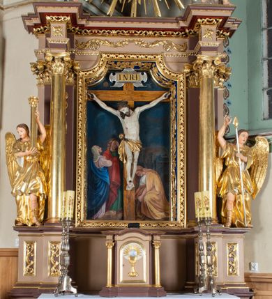 Zdjęcie nr 1: Nastawa ołtarzowa architektoniczna, jednoosiowa i jednokondygnacyjna. Ołtarz prostopadłościenny, drewniany, z drewnianą mensą i z marmurowym portatylem. Antepedium w formie prostokąta ujętego profilowaną ramą. W polu płycina o narożach zdobionych płaskorzeźbioną dekoracją roślinną złożoną z liści stylizowanego akantu oraz umieszczonym w polu veraikonem na tle obłoków i w promienistej glorii. Tabernakulum w kształcie prostopadłościennej skrzynki na niskim cokole, flankowane dwiema kolumnami ustawionymi pod kątem, zamknięte od góry prostym belkowaniem, pośrodku nadwieszonym. Na drzwiczkach płycina w kształcie stojącego prostokąta, zamkniętego łukiem półkolistym, ujęta profilowaną ramą, w polu której umieszczony jest płaskorzeźbiony kielich z hostią.

Retabulum ustawione na podwójnym cokole, flankowane parą zdwojonych pilastrów i ustawionych przed nimi dwiema kolumnami. Podpory dźwigają wyłamane na osi belkowanie z ustawionymi na bokach rzeźbami aniołków z arma Christi (włóczniami). Kolumny wspierają się na bazach, trzony mają gładkie i złocone, a kapitele kompozytowe. Po bokach ołtarza na niskich cokołach ustawione są rzeźby aniołów z narzędziami męki Pańskiej w dłoniach: kolumną biczowania po lewej stronie i włócznią po prawej stronie. W polu, w głębokiej wnęce ujętej szeroką, profilowaną ramą umieszczony jest późnobarokowy krucyfiks na tle malowanej Golgoty i postaci Matki Boskiej, św. Jana Ewangelisty i św. Weroniki. Wnęka od wewnątrz zdobiona jest płaskorzeźbioną winną latoroślą. Cokół dekorowany jest prostokątnymi po bokach płycinami, wypełnionymi stylizowanym akantem. Belkowanie zdobione wicią liści akantu, imposty rozetkami. W zwieńczeniu monumentalna promienista gloria złożona z wiązek promieni o nierównej długości z monogramem Chrystusa na niebieskim tle w polu, otoczonym wieńcem z obłoków. Struktura polichromowana w kolorze jasnego, delikatnego fioletu, płyciny, filary i detale w odcieniu delikatnie ciemniejszym; ornamentyka i profilowania złocone i srebrzone.


