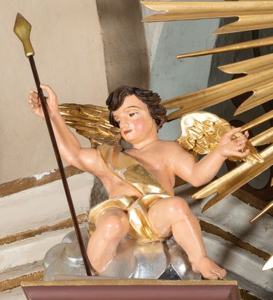 Zdjęcie nr 45: Nastawa ołtarzowa architektoniczna, jednoosiowa i jednokondygnacyjna. Ołtarz prostopadłościenny, drewniany, z drewnianą mensą i z marmurowym portatylem. Antepedium w formie prostokąta ujętego profilowaną ramą. W polu płycina o narożach zdobionych płaskorzeźbioną dekoracją roślinną złożoną z liści stylizowanego akantu oraz umieszczonym w polu veraikonem na tle obłoków i w promienistej glorii. Tabernakulum w kształcie prostopadłościennej skrzynki na niskim cokole, flankowane dwiema kolumnami ustawionymi pod kątem, zamknięte od góry prostym belkowaniem, pośrodku nadwieszonym. Na drzwiczkach płycina w kształcie stojącego prostokąta, zamkniętego łukiem półkolistym, ujęta profilowaną ramą, w polu której umieszczony jest płaskorzeźbiony kielich z hostią.

Retabulum ustawione na podwójnym cokole, flankowane parą zdwojonych pilastrów i ustawionych przed nimi dwiema kolumnami. Podpory dźwigają wyłamane na osi belkowanie z ustawionymi na bokach rzeźbami aniołków z arma Christi (włóczniami). Kolumny wspierają się na bazach, trzony mają gładkie i złocone, a kapitele kompozytowe. Po bokach ołtarza na niskich cokołach ustawione są rzeźby aniołów z narzędziami męki Pańskiej w dłoniach: kolumną biczowania po lewej stronie i włócznią po prawej stronie. W polu, w głębokiej wnęce ujętej szeroką, profilowaną ramą umieszczony jest późnobarokowy krucyfiks na tle malowanej Golgoty i postaci Matki Boskiej, św. Jana Ewangelisty i św. Weroniki. Wnęka od wewnątrz zdobiona jest płaskorzeźbioną winną latoroślą. Cokół dekorowany jest prostokątnymi po bokach płycinami, wypełnionymi stylizowanym akantem. Belkowanie zdobione wicią liści akantu, imposty rozetkami. W zwieńczeniu monumentalna promienista gloria złożona z wiązek promieni o nierównej długości z monogramem Chrystusa na niebieskim tle w polu, otoczonym wieńcem z obłoków. Struktura polichromowana w kolorze jasnego, delikatnego fioletu, płyciny, filary i detale w odcieniu delikatnie ciemniejszym; ornamentyka i profilowania złocone i srebrzone.


