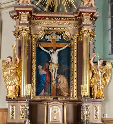Zdjęcie nr 16: Krucyfiks w typie Cristo morte; postać  Chrystusa umarłego przybitego do krzyża trzema gwoździami. Sylwetka w delikatnym zwisie, o silnie zaznaczonej anatomii ciała, z podkreśloną linią żeber i zaznaczonymi śladami męki. Perizonium w formie tkaniny przewiązanej na sznurze na prawym boku, sięgające kolan i odsłaniające prawe udo. Twarz Jezusa podłużna opadająca na prawe ramię, okolona zarostem; oczy zamknięte, nos podłużny, usta delikatnie otwarte; włosy długie spływające na prawe ramię, na głowie zielona korona cierniowa. Krzyż drewniany, prosty. Nad głową Chrystusa zawieszona tabliczka w kształcie kartusza zdobionego ornamentem okuciowym z napisem „I.N.R.I.” Partie ciała polichromowane naturalistycznie, perizonium złocone.




