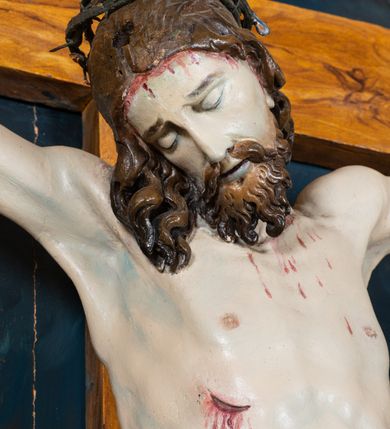 Zdjęcie nr 3: Krucyfiks w typie Cristo morte; postać  Chrystusa umarłego przybitego do krzyża trzema gwoździami. Sylwetka w delikatnym zwisie, o silnie zaznaczonej anatomii ciała, z podkreśloną linią żeber i zaznaczonymi śladami męki. Perizonium w formie tkaniny przewiązanej na sznurze na prawym boku, sięgające kolan i odsłaniające prawe udo. Twarz Jezusa podłużna opadająca na prawe ramię, okolona zarostem; oczy zamknięte, nos podłużny, usta delikatnie otwarte; włosy długie spływające na prawe ramię, na głowie zielona korona cierniowa. Krzyż drewniany, prosty. Nad głową Chrystusa zawieszona tabliczka w kształcie kartusza zdobionego ornamentem okuciowym z napisem „I.N.R.I.” Partie ciała polichromowane naturalistycznie, perizonium złocone.




