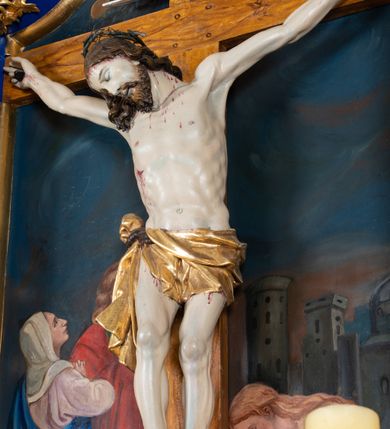 Zdjęcie nr 2: Krucyfiks w typie Cristo morte; postać  Chrystusa umarłego przybitego do krzyża trzema gwoździami. Sylwetka w delikatnym zwisie, o silnie zaznaczonej anatomii ciała, z podkreśloną linią żeber i zaznaczonymi śladami męki. Perizonium w formie tkaniny przewiązanej na sznurze na prawym boku, sięgające kolan i odsłaniające prawe udo. Twarz Jezusa podłużna opadająca na prawe ramię, okolona zarostem; oczy zamknięte, nos podłużny, usta delikatnie otwarte; włosy długie spływające na prawe ramię, na głowie zielona korona cierniowa. Krzyż drewniany, prosty. Nad głową Chrystusa zawieszona tabliczka w kształcie kartusza zdobionego ornamentem okuciowym z napisem „I.N.R.I.” Partie ciała polichromowane naturalistycznie, perizonium złocone.




