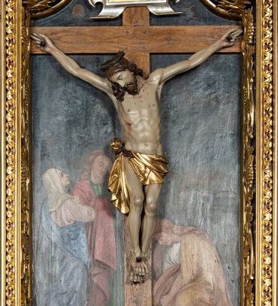 Zdjęcie nr 18: Krucyfiks w typie Cristo morte; postać  Chrystusa umarłego przybitego do krzyża trzema gwoździami. Sylwetka w delikatnym zwisie, o silnie zaznaczonej anatomii ciała, z podkreśloną linią żeber i zaznaczonymi śladami męki. Perizonium w formie tkaniny przewiązanej na sznurze na prawym boku, sięgające kolan i odsłaniające prawe udo. Twarz Jezusa podłużna opadająca na prawe ramię, okolona zarostem; oczy zamknięte, nos podłużny, usta delikatnie otwarte; włosy długie spływające na prawe ramię, na głowie zielona korona cierniowa. Krzyż drewniany, prosty. Nad głową Chrystusa zawieszona tabliczka w kształcie kartusza zdobionego ornamentem okuciowym z napisem „I.N.R.I.” Partie ciała polichromowane naturalistycznie, perizonium złocone.




