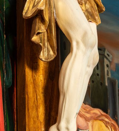 Zdjęcie nr 12: Krucyfiks w typie Cristo morte; postać  Chrystusa umarłego przybitego do krzyża trzema gwoździami. Sylwetka w delikatnym zwisie, o silnie zaznaczonej anatomii ciała, z podkreśloną linią żeber i zaznaczonymi śladami męki. Perizonium w formie tkaniny przewiązanej na sznurze na prawym boku, sięgające kolan i odsłaniające prawe udo. Twarz Jezusa podłużna opadająca na prawe ramię, okolona zarostem; oczy zamknięte, nos podłużny, usta delikatnie otwarte; włosy długie spływające na prawe ramię, na głowie zielona korona cierniowa. Krzyż drewniany, prosty. Nad głową Chrystusa zawieszona tabliczka w kształcie kartusza zdobionego ornamentem okuciowym z napisem „I.N.R.I.” Partie ciała polichromowane naturalistycznie, perizonium złocone.




