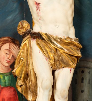 Zdjęcie nr 14: Krucyfiks w typie Cristo morte; postać  Chrystusa umarłego przybitego do krzyża trzema gwoździami. Sylwetka w delikatnym zwisie, o silnie zaznaczonej anatomii ciała, z podkreśloną linią żeber i zaznaczonymi śladami męki. Perizonium w formie tkaniny przewiązanej na sznurze na prawym boku, sięgające kolan i odsłaniające prawe udo. Twarz Jezusa podłużna opadająca na prawe ramię, okolona zarostem; oczy zamknięte, nos podłużny, usta delikatnie otwarte; włosy długie spływające na prawe ramię, na głowie zielona korona cierniowa. Krzyż drewniany, prosty. Nad głową Chrystusa zawieszona tabliczka w kształcie kartusza zdobionego ornamentem okuciowym z napisem „I.N.R.I.” Partie ciała polichromowane naturalistycznie, perizonium złocone.




