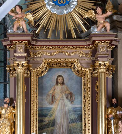 Zdjęcie nr 2: Nastawa ołtarzowa architektoniczna, jednoosiowa i jednokondygnacyjna. Ołtarz prostopadłościenny, drewniany z drewnianą mensą i z marmurowym portatylem. Antepedium w formie prostokąta ujętego profilowaną ramą. W polu płycina o narożach zdobionych płaskorzeźbioną dekoracją roślinną złożoną z liści stylizowanego akantu oraz umieszczonym w polu Barankiem Paschalnym na księdze z siedmioma pieczęciami na czerwonym tle w otoczeniu obłoków i promienistej glorii. Tabernakulum w kształcie prostopadłościennej skrzynki na niskim cokole, flankowane dwiema kolumnami ustawionymi pod kątem, zamknięte od góry prostym belkowaniem, pośrodku nadwieszonym. Na drzwiczkach płycina w kształcie stojącego prostokąta, zamkniętego łukiem półkolistym, ujęta profilowaną ramą, w polu umieszczony jest płaskorzeźbiony kielich z hostią.

Retabulum ustawione na podwójnym cokole, flankowane parą zdwojonych pilastrów i ustawionych przed nimi dwiema kolumnami. Podpory dźwigają wyłamane na osi belkowanie z ustawionymi na bokach rzeźbami aniołków, które trzymają w dłoniach pastorał oraz infułę. Kolumny wspierają się na bazach, trzony mają gładkie i złocone, a kapitele kompozytowe. Po bokach ołtarza na niskich cokołach ustawione są rzeźby: św. Piotra po lewej i św. Pawła po prawej stronie. W polu, w głębokiej wnęce ujętej szeroką, profilowaną ramą umieszczony jest obraz Najświętszego Serca Pana Jezusa. Wnęka od wewnątrz zdobiona płaskorzeźbioną winną latoroślą. Cokół dekorowany jest prostokątnymi płycinami, po bokach wypełnionymi stylizowanym akantem, a pośrodku gablotką z wotami. Belkowanie zdobione wicią z liści akantu oraz rozetami na impostach. W zwieńczeniu monumentalna promienista gloria złożona z wiązek promieni o nierównej długości z monogramem maryjnym na niebieskim tle w polu, otoczonym wieńcem z obłoków. Struktura polichromowana w kolorze jasnego, delikatnego fioletu, płyciny, filary i detale w odcieniu delikatnie ciemniejszym; ornamentyka i profilowania złocone i srebrzone.
