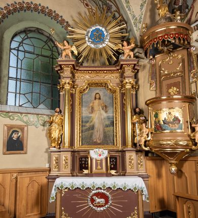 Zdjęcie nr 3: Nastawa ołtarzowa architektoniczna, jednoosiowa i jednokondygnacyjna. Ołtarz prostopadłościenny, drewniany z drewnianą mensą i z marmurowym portatylem. Antepedium w formie prostokąta ujętego profilowaną ramą. W polu płycina o narożach zdobionych płaskorzeźbioną dekoracją roślinną złożoną z liści stylizowanego akantu oraz umieszczonym w polu Barankiem Paschalnym na księdze z siedmioma pieczęciami na czerwonym tle w otoczeniu obłoków i promienistej glorii. Tabernakulum w kształcie prostopadłościennej skrzynki na niskim cokole, flankowane dwiema kolumnami ustawionymi pod kątem, zamknięte od góry prostym belkowaniem, pośrodku nadwieszonym. Na drzwiczkach płycina w kształcie stojącego prostokąta, zamkniętego łukiem półkolistym, ujęta profilowaną ramą, w polu umieszczony jest płaskorzeźbiony kielich z hostią.

Retabulum ustawione na podwójnym cokole, flankowane parą zdwojonych pilastrów i ustawionych przed nimi dwiema kolumnami. Podpory dźwigają wyłamane na osi belkowanie z ustawionymi na bokach rzeźbami aniołków, które trzymają w dłoniach pastorał oraz infułę. Kolumny wspierają się na bazach, trzony mają gładkie i złocone, a kapitele kompozytowe. Po bokach ołtarza na niskich cokołach ustawione są rzeźby: św. Piotra po lewej i św. Pawła po prawej stronie. W polu, w głębokiej wnęce ujętej szeroką, profilowaną ramą umieszczony jest obraz Najświętszego Serca Pana Jezusa. Wnęka od wewnątrz zdobiona płaskorzeźbioną winną latoroślą. Cokół dekorowany jest prostokątnymi płycinami, po bokach wypełnionymi stylizowanym akantem, a pośrodku gablotką z wotami. Belkowanie zdobione wicią z liści akantu oraz rozetami na impostach. W zwieńczeniu monumentalna promienista gloria złożona z wiązek promieni o nierównej długości z monogramem maryjnym na niebieskim tle w polu, otoczonym wieńcem z obłoków. Struktura polichromowana w kolorze jasnego, delikatnego fioletu, płyciny, filary i detale w odcieniu delikatnie ciemniejszym; ornamentyka i profilowania złocone i srebrzone.
