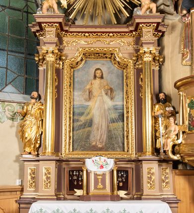 Zdjęcie nr 10: Nastawa ołtarzowa architektoniczna, jednoosiowa i jednokondygnacyjna. Ołtarz prostopadłościenny, drewniany z drewnianą mensą i z marmurowym portatylem. Antepedium w formie prostokąta ujętego profilowaną ramą. W polu płycina o narożach zdobionych płaskorzeźbioną dekoracją roślinną złożoną z liści stylizowanego akantu oraz umieszczonym w polu Barankiem Paschalnym na księdze z siedmioma pieczęciami na czerwonym tle w otoczeniu obłoków i promienistej glorii. Tabernakulum w kształcie prostopadłościennej skrzynki na niskim cokole, flankowane dwiema kolumnami ustawionymi pod kątem, zamknięte od góry prostym belkowaniem, pośrodku nadwieszonym. Na drzwiczkach płycina w kształcie stojącego prostokąta, zamkniętego łukiem półkolistym, ujęta profilowaną ramą, w polu umieszczony jest płaskorzeźbiony kielich z hostią.

Retabulum ustawione na podwójnym cokole, flankowane parą zdwojonych pilastrów i ustawionych przed nimi dwiema kolumnami. Podpory dźwigają wyłamane na osi belkowanie z ustawionymi na bokach rzeźbami aniołków, które trzymają w dłoniach pastorał oraz infułę. Kolumny wspierają się na bazach, trzony mają gładkie i złocone, a kapitele kompozytowe. Po bokach ołtarza na niskich cokołach ustawione są rzeźby: św. Piotra po lewej i św. Pawła po prawej stronie. W polu, w głębokiej wnęce ujętej szeroką, profilowaną ramą umieszczony jest obraz Najświętszego Serca Pana Jezusa. Wnęka od wewnątrz zdobiona płaskorzeźbioną winną latoroślą. Cokół dekorowany jest prostokątnymi płycinami, po bokach wypełnionymi stylizowanym akantem, a pośrodku gablotką z wotami. Belkowanie zdobione wicią z liści akantu oraz rozetami na impostach. W zwieńczeniu monumentalna promienista gloria złożona z wiązek promieni o nierównej długości z monogramem maryjnym na niebieskim tle w polu, otoczonym wieńcem z obłoków. Struktura polichromowana w kolorze jasnego, delikatnego fioletu, płyciny, filary i detale w odcieniu delikatnie ciemniejszym; ornamentyka i profilowania złocone i srebrzone.
