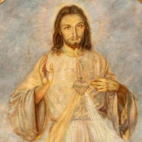 Zdjęcie nr 1: Obraz w kształcie stojącego prostokąta o wklęsłych górnych narożach z przedstawieniem Najświętszego Serca Jezusa. W centrum kompozycji ukazany jest Jezus w całej postaci, prawą ręką czyni gest błogosławieństwa, lewą wskazuje na gorejące na piersi serce. Twarz podłużna z długim i wąskim nosem, dużymi oczami, okolona krótką brodą, rozdzieloną na dwa, małe pukle. Włosy długie, ciemnobrązowe, z przedziałkiem pośrodku, opadające na plecy i ramiona bujnymi falami. Jezus ubrany jest w długą, jasną suknię, przewiązaną w talii. Na dłoniach i stopach ma widoczne ślady męki. Wokół głowy ma okrągły nimb. Od serca oplecionego koroną cierniową odchodzą dwa strumienie promieni, po lewej złoty, a po prawej biały. Chrystus ukazany został na kwitnącej łące, w oddali widoczny jest polny krajobraz i jasne niebo. Kolorystyka pastelowa, miękki i delikatny modelunek. W dolnej części kompozycji złota banderola z napisem „JEZU UFAM TOBIE”. W dolnym, lewym narożu sygnatura: „A(dolf) Hyła”, a po prawej data „1951”. Rama wnęki drewniana, szeroka, profilowana, zdobiona winną latoroślą. 

