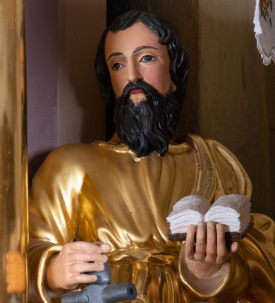 Zdjęcie nr 1: Rzeźba św. Pawła, drążona, ustawiona na niskim prostopadłościennym cokole w kolorze jasnobrązowym. Święty ustawiony frontalnie. W prawej ręce, ugiętej w łokciu trzyma miecz zwrócony ostrzem do dołu, a w lewej otwartą księgę. Twarz podłużna o wyrazistych rysach z długim nosem i małymi ustami, okolona długą i ciemną brodą oraz średniej długości włosami ułożonymi w pojedyncze kosmyki. Święty ubrany jest w długą, przewiązaną w pasie suknię i przerzucony przez lewe ramię złocony płaszcz. Na stopach ma złocone rzymskie sandały. Polichromia w odsłoniętych partiach ciała naturalistyczna. 


