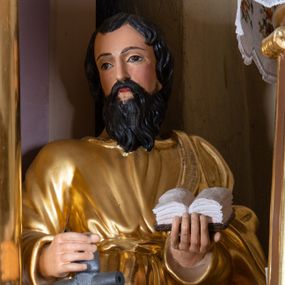 Zdjęcie nr 1: Rzeźba św. Pawła, drążona, ustawiona na niskim prostopadłościennym cokole w kolorze jasnobrązowym. Święty ustawiony frontalnie. W prawej ręce, ugiętej w łokciu trzyma miecz zwrócony ostrzem do dołu, a w lewej otwartą księgę. Twarz podłużna o wyrazistych rysach z długim nosem i małymi ustami, okolona długą i ciemną brodą oraz średniej długości włosami ułożonymi w pojedyncze kosmyki. Święty ubrany jest w długą, przewiązaną w pasie suknię i przerzucony przez lewe ramię złocony płaszcz. Na stopach ma złocone rzymskie sandały. Polichromia w odsłoniętych partiach ciała naturalistyczna. 


