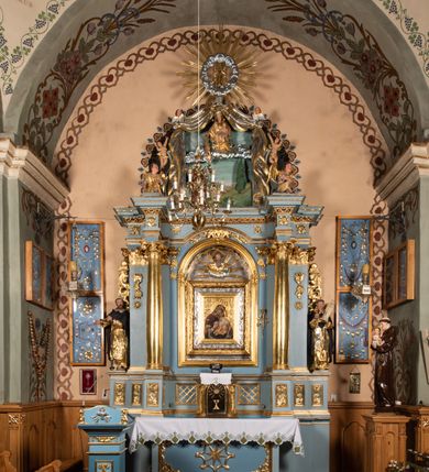 Zdjęcie nr 19: Ołtarz architektoniczny, jednoosiowy, jednokondygnacyjny ze zwieńczeniem. Mensa w kształcie nieregularnego prostopadłościanu, poprzedzona dwoma stopniami. Antepedium w formie prostokątnej płyciny, wewnątrz której w narożach są stylizowane dekoracje kwiatowe, a pośrodku równoramienna gwiazda w kartuszu. Tabernakulum w kształcie prostokątnej skrzynki, flankowane w narożach ustawionymi pod kątem pilastrami w formie liści, podtrzymującymi wyłamujący się gzyms. Drzwiczki zamknięte półkoliście z aplikowanym motywem kielicha oraz medalionem z napisem IHS w niewielkiej glorii. Drzwiczki obite srebrzoną blachą, boki i dekoracje złocone, gzyms w kolorze jasnoniebieskim. 

Cokół nastawy zdobiony kratkowaniem, a po bokach prostokątnymi płycinami ze stylizowaną dekoracją akantową. Retabulum flankowane zdwojoną parą pilastrów i stojącą przed nimi parą kolumn. Podpory dźwigają wyłamane na osi belkowanie. Kolumny ustawione na bazach, trzony gładkie i złocone, wybrzuszone pośrodku, kapitele kompozytowe. W polu głównym w niszy zamkniętej półkolistym łukiem umieszczony jest obraz Matki Boskiej z Dzieciątkiem, a powyżej rzeźba Boga Ojca. Na boku ołtarza znajdują się rzeźby: św. Dominika po lewej i św. Jacka po prawej stronie. Na belkowaniu usadzona jest para aniołków. Zwieńczenie o fantazyjnym kształcie zbliżonym do stojącego prostokąta z płaskorzeźbioną sceną ofiarowania szkaplerza św. Szymonowi Stockowi. U góry zwieńczenia podpięta srebrzona kotara o złoconym brzegu, spływająca na jego boki zwieńczenia. W górnej partii, po bokach para aniołków z wzniesionymi do góry rękami oraz dwie uskrzydlone główki anielskie. Na szczycie nastawy zatknięta jest promienista gloria złożona z wiązek promieni o nierównej długości z monogramem maryjnym otoczonym przez wieniec z obłoków w polu. Po bokach nastawy ołtarzowej umieszczone są uszaki utworzone ze stylizowanego akantu. Polichromia ołtarza w kolorze jasnoniebieskim, dekoracje ornamentalne oraz detale złocone i srebrzone. 
