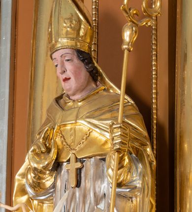 Zdjęcie nr 1: Rzeźba św. Stanisława z Piotrowiniem ścięta z tyłu i drążona, ustawiona na  ciemnozielonym cokole. Święty ukazany jest frontalnie w delikatnym kontrapoście z lewą nogą ugiętą w kolanie. Prawą dłonią czyni gest błogosławieństwa, a w lewej trzyma pastorał. Twarz podłużna o dużym nosie z silnie zaznaczonym podbródkiem, przymkniętych oczach, okolona średniej długości ciemnobrązowymi włosami zasłaniającymi uszy. Święty ubrany jest w srebrzoną albę i rokietę oraz w złocony mucet, kapę, rękawice i infułę; na szyi ma założony złocony krzyż pektoralny. Tkaniny są obficie drapowane w rurkowate i równoległe fałdy, u spodu łamane. U nóg św. Stanisława ukazana jest z lewego profilu półpostać nagiego, z czerwonym całunem przerzuconym przez ramię Piotrowina z uniesionymi rękami złożonymi w geście modlitwy. Sylwetka wychudzona, karnacja szara, głowa okolona częściowo łysiną. Polichromia naturalistyczna w odsłoniętych partiach ciała św. Stanisława.