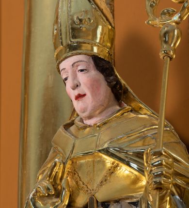 Zdjęcie nr 4: Rzeźba św. Stanisława z Piotrowiniem ścięta z tyłu i drążona, ustawiona na  ciemnozielonym cokole. Święty ukazany jest frontalnie w delikatnym kontrapoście z lewą nogą ugiętą w kolanie. Prawą dłonią czyni gest błogosławieństwa, a w lewej trzyma pastorał. Twarz podłużna o dużym nosie z silnie zaznaczonym podbródkiem, przymkniętych oczach, okolona średniej długości ciemnobrązowymi włosami zasłaniającymi uszy. Święty ubrany jest w srebrzoną albę i rokietę oraz w złocony mucet, kapę, rękawice i infułę; na szyi ma założony złocony krzyż pektoralny. Tkaniny są obficie drapowane w rurkowate i równoległe fałdy, u spodu łamane. U nóg św. Stanisława ukazana jest z lewego profilu półpostać nagiego, z czerwonym całunem przerzuconym przez ramię Piotrowina z uniesionymi rękami złożonymi w geście modlitwy. Sylwetka wychudzona, karnacja szara, głowa okolona częściowo łysiną. Polichromia naturalistyczna w odsłoniętych partiach ciała św. Stanisława.