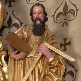 Zdjęcie nr 1: Rzeźba św. Tomasza ścięta z tyłu i drążona, ustawiona na półkolistym i zielonym cokole. Święty ukazany jest frontalnie, delikatnie pochylony w lewo. W prawej dłoni trzyma otwartą księgę, a W lewej ugiętej w łokciu węgielnicę. Twarz podłużna o dużym nosie i oczach, okolona długą i falistą brodą oraz półdługimi kręconymi włosami, zasłaniającymi uszy. Ubrany jest w długą suknię przewiązaną w talii z wąskimi rękawami i kołnierzykiem, zapiętą u góry na guziki, a także płaszcz zarzucony na ramiona i zawinięty wokół lewego przedramienia; stopy bose. Tkaniny są obficie drapowane w rurkowate i równoległe fałdy. Polichromia jest naturalistyczna w odsłoniętych partiach ciała, a szaty złocone.
