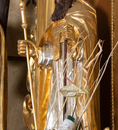 Zdjęcie nr 3: Rzeźba św. Wojciecha ścięta z tyłu i drążona, ustawiona na półkolistym i zielonym cokole. Święty ukazany jest frontalnie, w prawej dłoni trzyma krzyż, a w lewej wiosło. Twarz podłużna o dużym nosie i oczach, okolona długą i falistą brodą oraz półdługimi kręconymi włosami, zasłaniającymi uszy. Ubrany jest w srebrzoną albę i rokietę oraz w złocony paliusz, mucet, kapę, rękawice i infułę; na stopach ma założone czarne, pełne buty. Tkaniny są obficie drapowane w rurkowate i równoległe fałdy, u spodu łamane. Polichromia jest naturalistyczna w odsłoniętych partiach ciała.











