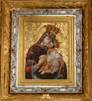 Zdjęcie nr 2: Obraz Matki Boskiej z Dzieciątkiem w kształcie stojącego prostokąta. Maria ukazana w półpostaci, delikatnie zwrócona w lewo z Dzieciątkiem Jezus na lewym ręku, z głową przytuloną do jego twarzy, prawą dłonią trzymająca jego lewą rączkę. Twarz Marii pełna, nos długi, duże i brązowe oczy oraz drobne usta. Ubrana jest w niebieską suknię z długimi rękawami, ozdobioną na brzegu złoconą bordiurą oraz ciemnoczerwony maforion , malowanym światłocieniowo z zieloną podszewką i z lewą połą zarzuconą na prawe ramię. Płaszcz ozdobiony jest trzema gwiazdami: na czole, na dekolcie po lewej stronie i na prawym ramieniu; a na brzegach dekorowany jest ozdobną lamówką z filigranowymi frędzlami. Dzieciątko siedzi na ramieniu Matki, zwrócone trzy czwarte w prawo, ma skrzyżowane nóżki, a lewą rękę trzyma w prawej dłoni Matki Boskiej. Ubrane jest w srebrną sukienkę z długimi i szerokimi rękawami, przewiązaną w talii jasnobeżową tkaniną oraz złoconą szatę wierzchnią, bez rękawów, skrzyżowaną na piersi, ozdobioną szrafowaniem. Twarz Jezusa pełna o pucułowatych policzkach i podkreślonych podbródku z długim nosem, małymi ustami i dużymi ciemnymi oczami. Karnacje obu postaci ciemne z zarumienionymi policzkami. Na głowach mają założone pełne korony zdobione fioletowymi, niebieskimi i czerwonymi kamieniami; a wokół głów koliste i złocone nimby. Na wysokości głowy Matki Bożej, po lewej stronie znajdują się tłoczone abrewiacje: „MP ΘY”, a po prawej: „IX XC”.  Ornament tła wyciskany w gruncie, złocony o układzie kandelabrowym, roślinnym z motyw palmetowym. Na odwrociu napis: „obraz podług trad(ycji) z IX w(wieku) konserw(owany) z XIV w(ieku), odnow(iony) i zakonserw(owany) 1963 kons(erwator) Zawadzki T(adeusz) Dzierża z Kr(akowa) Prob(oszcz) X(iądz) J(ózef) Długopolski kość. Mika Fr.” Wizerunek umieszczony jest w złoconej, profilowanej ramie, od wewnątrz zdobionej pasem kimationu.

