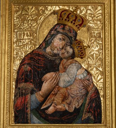 Zdjęcie nr 7: Obraz Matki Boskiej z Dzieciątkiem w kształcie stojącego prostokąta. Maria ukazana w półpostaci, delikatnie zwrócona w lewo z Dzieciątkiem Jezus na lewym ręku, z głową przytuloną do jego twarzy, prawą dłonią trzymająca jego lewą rączkę. Twarz Marii pełna, nos długi, duże i brązowe oczy oraz drobne usta. Ubrana jest w niebieską suknię z długimi rękawami, ozdobioną na brzegu złoconą bordiurą oraz ciemnoczerwony maforion , malowanym światłocieniowo z zieloną podszewką i z lewą połą zarzuconą na prawe ramię. Płaszcz ozdobiony jest trzema gwiazdami: na czole, na dekolcie po lewej stronie i na prawym ramieniu; a na brzegach dekorowany jest ozdobną lamówką z filigranowymi frędzlami. Dzieciątko siedzi na ramieniu Matki, zwrócone trzy czwarte w prawo, ma skrzyżowane nóżki, a lewą rękę trzyma w prawej dłoni Matki Boskiej. Ubrane jest w srebrną sukienkę z długimi i szerokimi rękawami, przewiązaną w talii jasnobeżową tkaniną oraz złoconą szatę wierzchnią, bez rękawów, skrzyżowaną na piersi, ozdobioną szrafowaniem. Twarz Jezusa pełna o pucułowatych policzkach i podkreślonych podbródku z długim nosem, małymi ustami i dużymi ciemnymi oczami. Karnacje obu postaci ciemne z zarumienionymi policzkami. Na głowach mają założone pełne korony zdobione fioletowymi, niebieskimi i czerwonymi kamieniami; a wokół głów koliste i złocone nimby. Na wysokości głowy Matki Bożej, po lewej stronie znajdują się tłoczone abrewiacje: „MP ΘY”, a po prawej: „IX XC”.  Ornament tła wyciskany w gruncie, złocony o układzie kandelabrowym, roślinnym z motyw palmetowym. Na odwrociu napis: „obraz podług trad(ycji) z IX w(wieku) konserw(owany) z XIV w(ieku), odnow(iony) i zakonserw(owany) 1963 kons(erwator) Zawadzki T(adeusz) Dzierża z Kr(akowa) Prob(oszcz) X(iądz) J(ózef) Długopolski kość. Mika Fr.” Wizerunek umieszczony jest w złoconej, profilowanej ramie, od wewnątrz zdobionej pasem kimationu.

