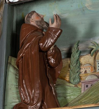 Zdjęcie nr 4: Zwieńczenie ołtarza o fantazyjnym kształcie zbliżonym do stojącego prostokąta z płaskorzeźbioną sceną ofiarowania szkaplerza św. Szymonowi Stockowi. U góry zwieńczenia podpięta srebrzona kotara o złoconym brzegu, spływająca na jego boki. W górnej partii, po bokach para aniołków z wzniesionymi do góry rękami oraz dwie uskrzydlone główki anielskie. Na szczycie nastawy zatknięta jest promienista gloria złożona z wiązek promieni o nierównej długości z monogramem maryjnym otoczonym przez wieniec z obłoków. Pole zwieńczenia dwustrefowe, oddzielone pasem obłoków. W dolnej strefie, po lewej stronie rzeźba św. Szymona Stocka. Święty ukazany jest w pozycji klęczącej z prawego profilu z wniesionymi na wysokości piersi rękami i głową skierowaną ku Matce Bożej. Twarz podłużna z długim nosem i silnie zarumienionymi policzkami. Głowę okala długa i siwa broda oraz tonsura. Święty ubrany jest w brązowy habit i płaszcz karmelitański. Po prawej stronie obrazu płaskorzeźbione, zielone wzniesienia i duże drzewo. W tle malowany pejzaż miejski i jasnobłękitne niebo. W górnej strefie siedząca na obłokach Matka Boska z Dzieciątkiem. W prawej dłoni trzyma szkaplerze zdobione greckim krzyżykiem oraz gorejącym sercem, przebitym mieczem, a lewą ręką przytrzymuje siedzące na jej kolanach Dzieciątko Jezus. Maria ma podłużną twarz z niewielkimi ustami, długim nosem i jasnoniebieskimi oczami, okoloną ciemnobrązowymi włosami, opadającymi na plecy. Ubrana jest w złocone szaty: suknię i płaszcz, obficie drapowane. Na głowie ma założony srebrzony welon oraz pełną koronę, a wokół niej wieniec z 12 gwiazd. Polichromia struktury zwieńczenia w kolorze jasnoniebieskim, dekoracje ornamentalne oraz detale złocone i srebrzone. Polichromia w odsłoniętych partiach ciała figur naturalistyczna.

