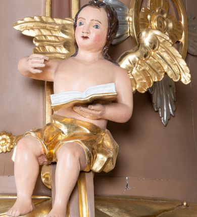 Zdjęcie nr 12: Ambona wisząca, przyścienna z wejściem od strony  kaplicy po północnej stronie prezbiterium. Kosz na planie półkolistym, na profilowanym cokole, z szyszką u spodu, flankowany po bokach dwoma spływami wolutowymi, na których ustawione są rzeźby siedzących aniołków. Na ściance kosza w profilowanej, złoconej ramie płaskorzeźba z przedstawieniem Połowu ryb. Zaplecek w kształcie prostokąta stojącego ujęty po bokach tkaniną przewiązaną u góry; w polu przedzielony złoconymi pasami ułożonymi na kształt litery H. W dolnej części zdobiony prostokątną płyciną ozdobioną płaskorzeźbioną rozetą, w górnej partii fantazyjną wicią roślinną. Baldachim  o wykroju półkolistym, w strefie belkowania zdobiony prostym fryzem przedzielonym pionowymi paskami na małe prostokątne płyciny, od dołu zdobiony lambrekinem, z dwoma wazonami płomienistymi z przodu oraz rzeźbą Mojżesza na skale w zwieńczeniu. U spodu baldachimu Gołębica Ducha Świętego w promienistej glorii złożonej z wiązek promieni o nierównej długości.
Płaskorzeźba na ściance frontowej kosza z przedstawieniem Połowu ryb. Kompozycja wielopostaciowa z ukazaniem po prawej stronie Jezusa nauczającego w łodzi oraz trzech uczniów wyciągających sieć pełną ryb. Po lewej stronie na brzegu siedząca postać jednego z uczniów. Uczniowie ubrani w długie suknie z długimi rękawami w kolorach: czerwonym, niebieskim i zielonym. Jezus ubrany jest w długą, złotą suknię z długim rękawem i złoty płaszcz. Krajobraz ukazany sumarycznie z wyraźnie zaznaczonymi falami morskimi. Tło złocone, ze złoconymi obłokami.
Aniołki siedzące na wolutach ukazane frontalnie, z  rozpostartymi szeroko skrzydłami. Aniołek po lewej stronie z rękami lekko ugiętymi w łokciach, z zamkniętą księgą w lewej dłoni. Aniołek po prawej stronie, delikatnie przechylony w lewo, z otwartą księgą w lewej dłoni i prawą ręką uniesioną nad księgą. Aniołki przepasane w pasie złotą chustą. Twarze szerokie, z pucułowatymi i delikatnie zarumienionymi policzkami, małe i wąskie usta, krótkie nosy. Włosy średniej długości, ciemnobrązowe, kędzierzawe.
W zwieńczeniu na wysokiej skale ustawiona jest rzeźba Mojżesza, ukazana frontalnie, z lewą nogą wspartą na skale, z tablicą przykazań w lewym ręku i laską w prawej. Mojżesz ubrany w długą, złotą suknię z długim rękawem. Twarz podłużna, okolona długą, ciemnobrązową brodą i krótkimi, ciemnobrązowymi włosami.
Struktura ambony polichromowana w kolorze jasnobrązowym, detale w kolorze ciemnobrązowym,  profile i ornamenty złocone oraz posrebrzone.