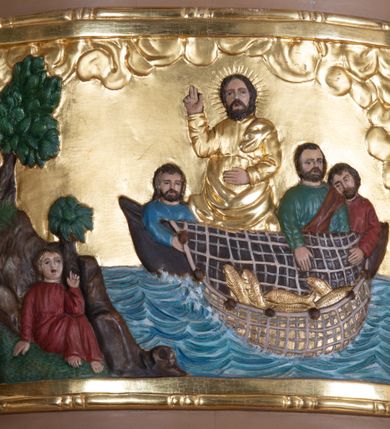 Zdjęcie nr 9: Ambona wisząca, przyścienna z wejściem od strony  kaplicy po północnej stronie prezbiterium. Kosz na planie półkolistym, na profilowanym cokole, z szyszką u spodu, flankowany po bokach dwoma spływami wolutowymi, na których ustawione są rzeźby siedzących aniołków. Na ściance kosza w profilowanej, złoconej ramie płaskorzeźba z przedstawieniem Połowu ryb. Zaplecek w kształcie prostokąta stojącego ujęty po bokach tkaniną przewiązaną u góry; w polu przedzielony złoconymi pasami ułożonymi na kształt litery H. W dolnej części zdobiony prostokątną płyciną ozdobioną płaskorzeźbioną rozetą, w górnej partii fantazyjną wicią roślinną. Baldachim  o wykroju półkolistym, w strefie belkowania zdobiony prostym fryzem przedzielonym pionowymi paskami na małe prostokątne płyciny, od dołu zdobiony lambrekinem, z dwoma wazonami płomienistymi z przodu oraz rzeźbą Mojżesza na skale w zwieńczeniu. U spodu baldachimu Gołębica Ducha Świętego w promienistej glorii złożonej z wiązek promieni o nierównej długości.
Płaskorzeźba na ściance frontowej kosza z przedstawieniem Połowu ryb. Kompozycja wielopostaciowa z ukazaniem po prawej stronie Jezusa nauczającego w łodzi oraz trzech uczniów wyciągających sieć pełną ryb. Po lewej stronie na brzegu siedząca postać jednego z uczniów. Uczniowie ubrani w długie suknie z długimi rękawami w kolorach: czerwonym, niebieskim i zielonym. Jezus ubrany jest w długą, złotą suknię z długim rękawem i złoty płaszcz. Krajobraz ukazany sumarycznie z wyraźnie zaznaczonymi falami morskimi. Tło złocone, ze złoconymi obłokami.
Aniołki siedzące na wolutach ukazane frontalnie, z  rozpostartymi szeroko skrzydłami. Aniołek po lewej stronie z rękami lekko ugiętymi w łokciach, z zamkniętą księgą w lewej dłoni. Aniołek po prawej stronie, delikatnie przechylony w lewo, z otwartą księgą w lewej dłoni i prawą ręką uniesioną nad księgą. Aniołki przepasane w pasie złotą chustą. Twarze szerokie, z pucułowatymi i delikatnie zarumienionymi policzkami, małe i wąskie usta, krótkie nosy. Włosy średniej długości, ciemnobrązowe, kędzierzawe.
W zwieńczeniu na wysokiej skale ustawiona jest rzeźba Mojżesza, ukazana frontalnie, z lewą nogą wspartą na skale, z tablicą przykazań w lewym ręku i laską w prawej. Mojżesz ubrany w długą, złotą suknię z długim rękawem. Twarz podłużna, okolona długą, ciemnobrązową brodą i krótkimi, ciemnobrązowymi włosami.
Struktura ambony polichromowana w kolorze jasnobrązowym, detale w kolorze ciemnobrązowym,  profile i ornamenty złocone oraz posrebrzone.