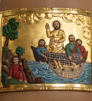 Zdjęcie nr 8: Ambona wisząca, przyścienna z wejściem od strony  kaplicy po północnej stronie prezbiterium. Kosz na planie półkolistym, na profilowanym cokole, z szyszką u spodu, flankowany po bokach dwoma spływami wolutowymi, na których ustawione są rzeźby siedzących aniołków. Na ściance kosza w profilowanej, złoconej ramie płaskorzeźba z przedstawieniem Połowu ryb. Zaplecek w kształcie prostokąta stojącego ujęty po bokach tkaniną przewiązaną u góry; w polu przedzielony złoconymi pasami ułożonymi na kształt litery H. W dolnej części zdobiony prostokątną płyciną ozdobioną płaskorzeźbioną rozetą, w górnej partii fantazyjną wicią roślinną. Baldachim  o wykroju półkolistym, w strefie belkowania zdobiony prostym fryzem przedzielonym pionowymi paskami na małe prostokątne płyciny, od dołu zdobiony lambrekinem, z dwoma wazonami płomienistymi z przodu oraz rzeźbą Mojżesza na skale w zwieńczeniu. U spodu baldachimu Gołębica Ducha Świętego w promienistej glorii złożonej z wiązek promieni o nierównej długości.
Płaskorzeźba na ściance frontowej kosza z przedstawieniem Połowu ryb. Kompozycja wielopostaciowa z ukazaniem po prawej stronie Jezusa nauczającego w łodzi oraz trzech uczniów wyciągających sieć pełną ryb. Po lewej stronie na brzegu siedząca postać jednego z uczniów. Uczniowie ubrani w długie suknie z długimi rękawami w kolorach: czerwonym, niebieskim i zielonym. Jezus ubrany jest w długą, złotą suknię z długim rękawem i złoty płaszcz. Krajobraz ukazany sumarycznie z wyraźnie zaznaczonymi falami morskimi. Tło złocone, ze złoconymi obłokami.
Aniołki siedzące na wolutach ukazane frontalnie, z  rozpostartymi szeroko skrzydłami. Aniołek po lewej stronie z rękami lekko ugiętymi w łokciach, z zamkniętą księgą w lewej dłoni. Aniołek po prawej stronie, delikatnie przechylony w lewo, z otwartą księgą w lewej dłoni i prawą ręką uniesioną nad księgą. Aniołki przepasane w pasie złotą chustą. Twarze szerokie, z pucułowatymi i delikatnie zarumienionymi policzkami, małe i wąskie usta, krótkie nosy. Włosy średniej długości, ciemnobrązowe, kędzierzawe.
W zwieńczeniu na wysokiej skale ustawiona jest rzeźba Mojżesza, ukazana frontalnie, z lewą nogą wspartą na skale, z tablicą przykazań w lewym ręku i laską w prawej. Mojżesz ubrany w długą, złotą suknię z długim rękawem. Twarz podłużna, okolona długą, ciemnobrązową brodą i krótkimi, ciemnobrązowymi włosami.
Struktura ambony polichromowana w kolorze jasnobrązowym, detale w kolorze ciemnobrązowym,  profile i ornamenty złocone oraz posrebrzone.