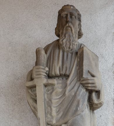 Zdjęcie nr 1: Rzeźba przedstawiająca św. Pawła, pełna, ustawiona na prostopadłościennym cokole. Święty ukazany w delikatnym kontrapoście z lewą nogą ugiętą w kolanie, z mieczem w prawej dłoni i księgą w lewej. Twarz podłużna, okolona długą brodą, usta delikatnie rozchylone, nos długi i prosty, włosy krótkie. Święty ubrany jest w długą suknię z długimi rękawami, przewiązaną w talii oraz płaszcz przerzucony przez prawe ramię i spływający połą z przodu na lewe ramię. Draperia szat sztywna, biegnąca równoległymi fałdami w dół. 