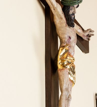 Zdjęcie nr 3: Rzeźba pełnoplastyczna przedstawiająca Chrystusa zawieszonego na krzyżu na wyprostowanych ramionach, figura w typie Cristo vivo. Głowa  Chrystusa delikatnie przechylona na prawe ramię; nogi wyprostowane w kolanach, stopy przebite jednym gwoździem w układzie prawa na lewą. Twarz Zbawiciela szeroka o wyraźnych rysach, długim i wąskim nosie oraz krótkiej brodzie, zawiniętej na końcu w dwa krótkie i silnie skręcone pukle. Włosy długie, opadające na plecy z jednym długim puklem spływającym sztywno na prawe ramię. Na głowie Chrystus ma założoną ciasno splecioną, zieloną koronę cierniową, zawiązaną opaską z gałązek. Sylwetka wychudzona, ułożona w nienaturalnej pozie z dużymi dłońmi i stopami. Perizonium złocone, ciasno oplatające biodra, przewiązane pośrodku z jednym końcem wystającym z prawej strony. Nad głową Chrystusa znajduje się titulus w formie białej tabliczki namalowanej na wolutowo wyciętym kartuszu z napisem w polu „I(ESUS) N(AZARENUS) R(EX) I[UDAEORUM]”. Polichromia naturalistyczna w odsłoniętych partiach ciała z zaznaczonymi śladami męki. Krzyż drewniany, prosty, malowany na kolor ciemnobrązowy.