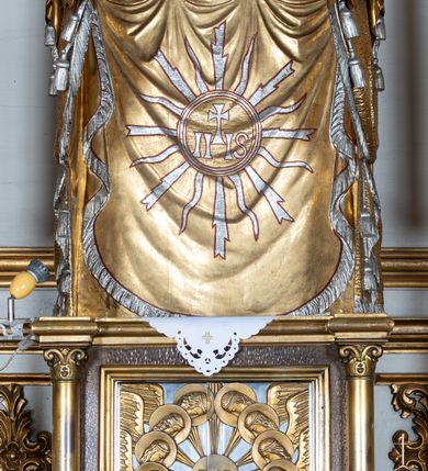 Zdjęcie nr 3: Mensa ołtarzowa kamienna, wsparta na dwóch konsolach, o profilowanym brzegu z inskrypcją „S[AN]CTI MARTYRES ADALBERTE EPISCOPE ET ANDREA SACERDOS ORATE PRO NOBIS”. Tabernakulum w formie drewnianej, prostopadłościennej skrzynki obitej fakturowaną blachą. Ścianka frontowa ujęta parą kolumienek, podtrzymujących niepełne belkowanie; drzwiczki dwuskrzydłowe z aplikowanymi aniołami otaczającymi hostię w glorii. Tron wystawienia drewniany, w formie baldachimu podtrzymywanego na tylnej ściance, z upiętymi po bokach kotarami z frędzlami i chwostami.

Nastawa ołtarzowa architektoniczna, jednoosiowa, jednokondygnacyjna ze zwieńczeniem, ustawiona na dwustrefowym cokole, dolnym murowanym. Kondygnacja ujęta dwiema parami pilastrów o kanelowanych trzonach i stylizowanych kapitelach kompozytowych, na tle skrajnej pary dwie kolumny o kapitelach kompozytowych. Podpory wspierają pełne belkowanie wyłamane na ich osi oraz przerwany, półkolisty przyczółek na osi zewnętrznej pary. W polu środkowym płytka nisza w formie stojącego prostokąta zamknięta łukiem odcinkowym nadwieszonym, ujęta profilowaną ramą z wpisaną ornamentalną ramą, wewnątrz znacznie mniejszy obraz w formie stojącego prostokąta z przedstawieniem Matki Boskiej z Dzieciątkiem. Zwieńczenie ustawione na niewielkim cokole, w formie stojącego prostokąta flankowanego parą kanelowanych pilastrów i stojącą przed nimi parą kolumienek, wspierających imposty z wazonami, zamkniętego dwoma falistymi i przeciwstawnie zwróconymi fragmentami gzymsu przechodzącymi w woluty; całość zakończona ornamentalnym szczytem z medalionem. W polu profilowana rama w formie stojącego prostokąta zamkniętego łukiem półkolistym nadwieszonym z przedstawieniem św. Jana Chrzciciela jako dziecka. Górna strefa cokołu oraz fryz dekorowane płycinami z ornamentem roślinnym. W przestrzeni pomiędzy pilastrami kondygnacji zwisy utworzone z pęków owoców i kwiatów, zawieszone na muszli. Struktura polichromowana w kolorze białym, kolumny, profile i ornamentyka złocone.