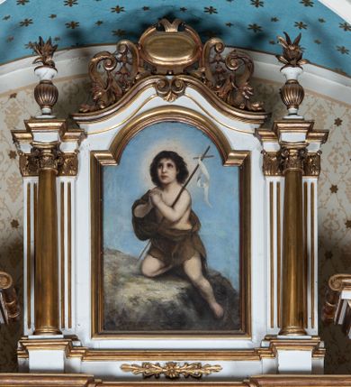 Zdjęcie nr 1: Obraz w  kształcie stojącego prostokąta zamkniętego od góry łukiem nadwieszonym. W centrum kompozycji ukazany św. Jan Chrzciciel jako dziecko. Święty zwrócony trzy czwarte w prawo, z prawą nogą podwiniętą, ze złożonymi w geście modlitwy rękami, lewą wyprostowaną, ułożoną w dół skały. Na lewym ramieniu świętego wsparty gładki krzyż o cienkim drzewcu z przewieszoną białą wstęgą. Święty ubrany jest w skórę, założoną na prawe ramię i przewiązaną na lewym boku. Twarz owalna z długim i prostym nosem, wzrokiem skierowanym ku górze. Głowa okolona bujnymi, ciemnymi i kędzierzawymi włosami, wokół niej nimb w formie jasnożółtego otoku. Tło obrazu jednolite, błękitne. Rama drewniana, profilowana i złocona.