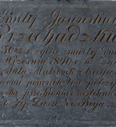 Zdjęcie nr 2: Epitafium w kształcie leżącego prostokąta, zwieńczone krzyżykiem na półkolistej stopie z ramionami w formie spłaszczonych kół. W narożach umieszczone są wielopłatkowe kwiatki, a w polu złocona inskrypcja „D(eo) O(ptimo) M(aximo) / Emilij z Jasińskich / Przechadzkiej / w 30ym r(oku) życia zmarłej, dnia / 2go Września 1840 r(oku) w Żalu / pozostały Małżonek z troigiem / dziecmi pomnik ten położył / z proźbą przechodnia o westchnienie / za Jej Duszę do Boga.”