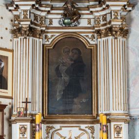 Zdjęcie nr 1: Nastawa ołtarzowa architektoniczna, jednoosiowa, jednokondygnacyjna ze zwieńczeniem, ustawiona na trójstrefowym cokole, dolnym murowanym. Mensa ołtarzowa kamienna, wsparta na dwóch konsolach, o profilowanym brzegu z inskrypcją „S(ANC)TI MART(YRES) STANISLAE EP(ISCOPE) CRACOVIAEN(SI) ET THOMA EP(ISCOPE) CANTUARIEN(SI) ORATE PRO NOBIS”. Tabernakulum w formie  drewnianej, prostopadłościennej skrzynki, ustawione na niskim cokole, zamknięte niewielkim gzymsem. Drzwiczki dwuskrzydłowe z aplikowanymi literami alfa i omega. Cokół nastawy zdobiony w dolnej partii parą konsolek z liśćmi akantu, powyżej prostokątne płyciny z rzeźbionymi główkami aniołków. Pośrodku cokół dekorowany prostokątną płyciną zamkniętą łukiem dwuramiennym z uskokiem. W polu płaskorzeźbiona dekoracja złożona z korony cierniowej na tle promienistej glorii oraz stylizowanych wici roślinnych akantu oraz rocaille’u.

Kondygnacja ujęta zwielokrotnionymi parami pilastrów o kanelowanych trzonach i stylizowanych kapitelach kompozytowych. Podpory wspierają pełne belkowanie wyłamane na ich osi oraz przerwany, półkolisty przyczółek na osi zewnętrznej. W polu środkowym płytka nisza w formie stojącego prostokąta zamknięta łukiem odcinkowym nadwieszonym, ujęta profilowaną ramą, wewnątrz obraz z przedstawieniem św. Antoniego Padewskiego. Zwieńczenie ustawione na niewielkim cokole, w formie stojącego prostokąta flankowanego parą kanelowanych pilastrów, wspierających profilowany gzyms i ustawione po bokach wazony. Całość zakończona ornamentalnym szczytem ze stylizowaną muszlą palmetową. W polu płaskorzeźbiona gołębica Ducha Świętego na tle promienistej glorii. Poniżej w partii fryzu rzeźba Boga Ojca. Po bokach zwieńczenia spływy wolutowe ozdobione kampanulami. Struktura polichromowana w kolorze białym, kolumny, profile i ornamentyka złocone, detale srebrzone.
