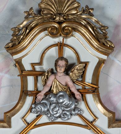 Zdjęcie nr 4: Oprawa chrzcielnicy architektoniczna jednoosiowa, jednokondygnacyjna ze zwieńczeniem, ustawiona na czterostrefowym cokole wyłamanym na osi podpór, w środkowej przestrzeni chrzcielnica; w drugiej od dołu strefie silnie wysunięte do przodu wsporniki podtrzymywane przez konsole dekorowane liśćmi akantu; trzy strefy cokołu zdobione płycinami. Kondygnacja węższa od podstawy, ujęta parą pilastrów o kanelowanych trzonach i kapitelach kompozytowych wspierających pełne belkowanie wyłamane na ich osi, nad polem środkowym przyjmujące kształt łuku odcinkowego. W polu środkowym płycina ujęta profilowaną ramą w formie stojącego prostokąta zamkniętego łukiem półkolistym nadwieszonym z uskokiem z płaskorzeźbioną sceną Chrztu Chrystusa z sygnaturą „1885 / P(AWEŁ) TURBAS”. Kondygnacja ujęta uszami utworzonymi z wici roślinnej z kwiatami. Zwieńczenie w formie stojącego prostokąta o wklęsłych bokach przechodzących w duże woluty spływające na belkowanie, zamknięte dwoma falistymi fragmentami gzymsu przechodzącymi w przeciwstawnie zwrócone woluty; całość zakończona szczytem utworzonym z muszli flankowanej kwiatowymi festonami. W polu płycina w formie zbliżonej do zwieńczenia z płaskorzeźbioną półpostacią aniołka na obłoku, z rękoma rozłożonymi na boki. Struktura polichromowana w kolorze białym ze złoconymi profilami i ornamentyką oraz srebrzoną płaskorzeźbą. 